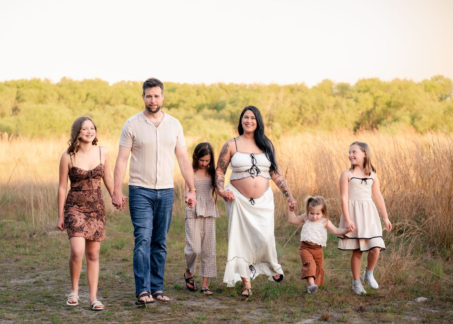 Family walking hand in hand through the open fields during a maternity session at Lake Runnymede Conservation Area St Cloud Florida