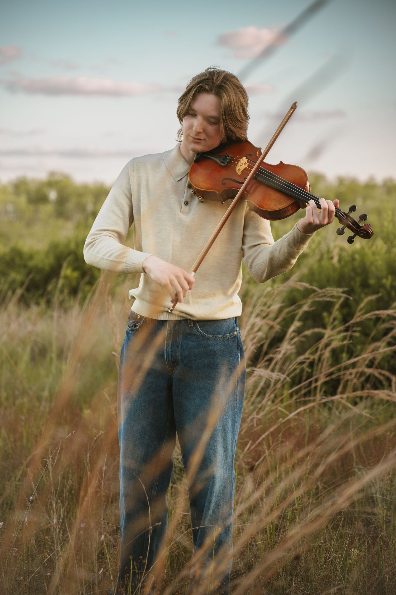 High school senior playing the violin against blue sky at graduation portrait session at Lake Runnymede Conservation Area St. Cloud Florida
