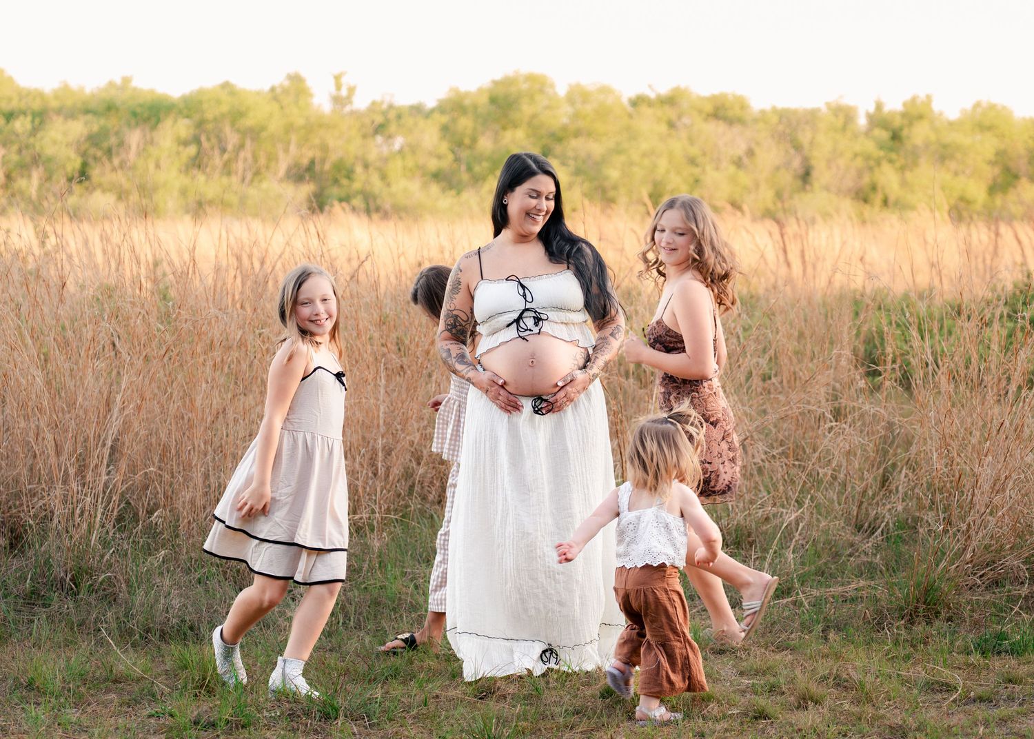 Mother laughing as her daughters run around her in the open fields of Lake Runnymede Conservation Area during their maternity session.