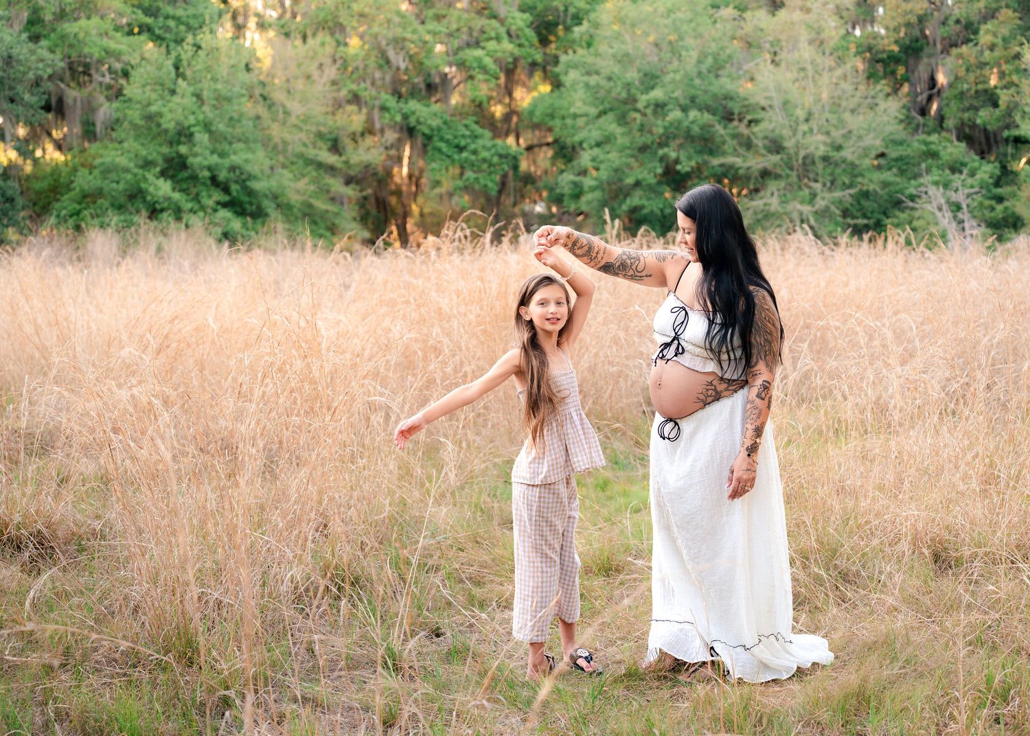 Expecting mother twirling her daughter beneath in tall grass during maternity session at Lake Runnymede Conservation Area in St Cloud FL