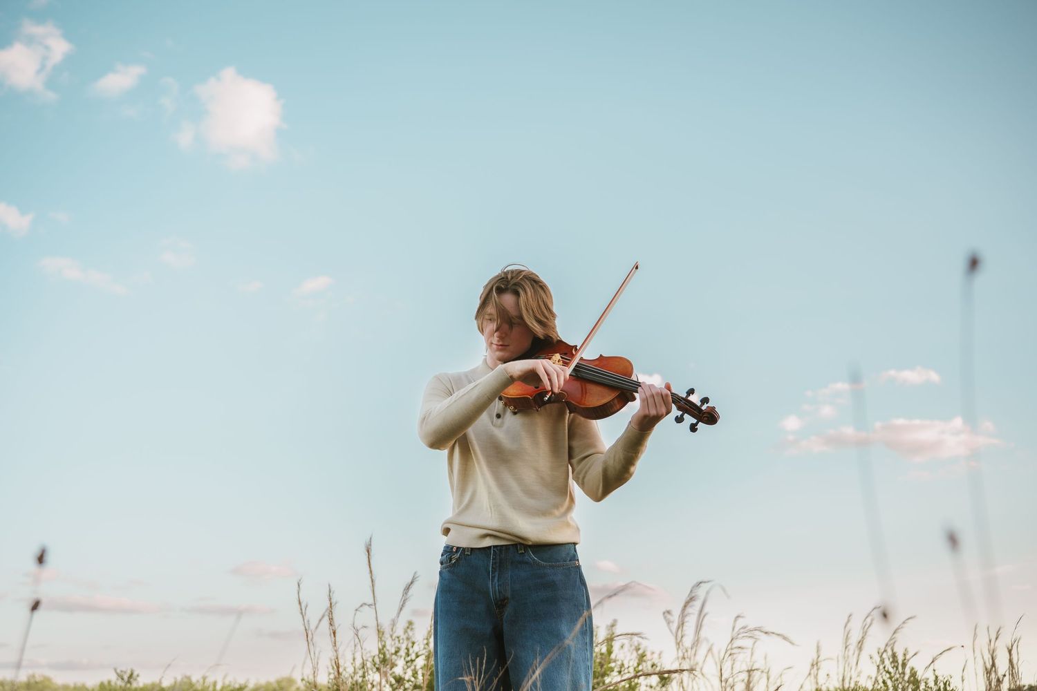 High school senior playing the violin against blue sky at graduation portrait session at Lake Runnymede Conservation Area St. Cloud Florida