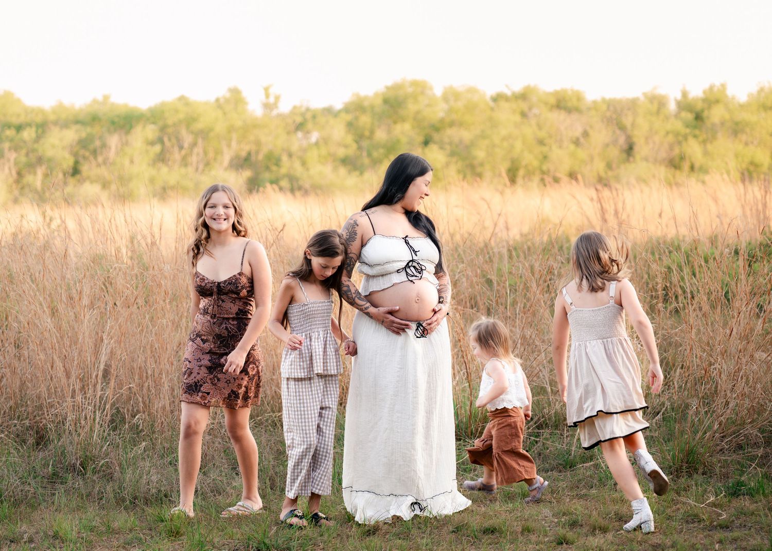 Mother laughing as her daughters run around her in the open fields of Lake Runnymede Conservation Area during maternity session St Cloud FL