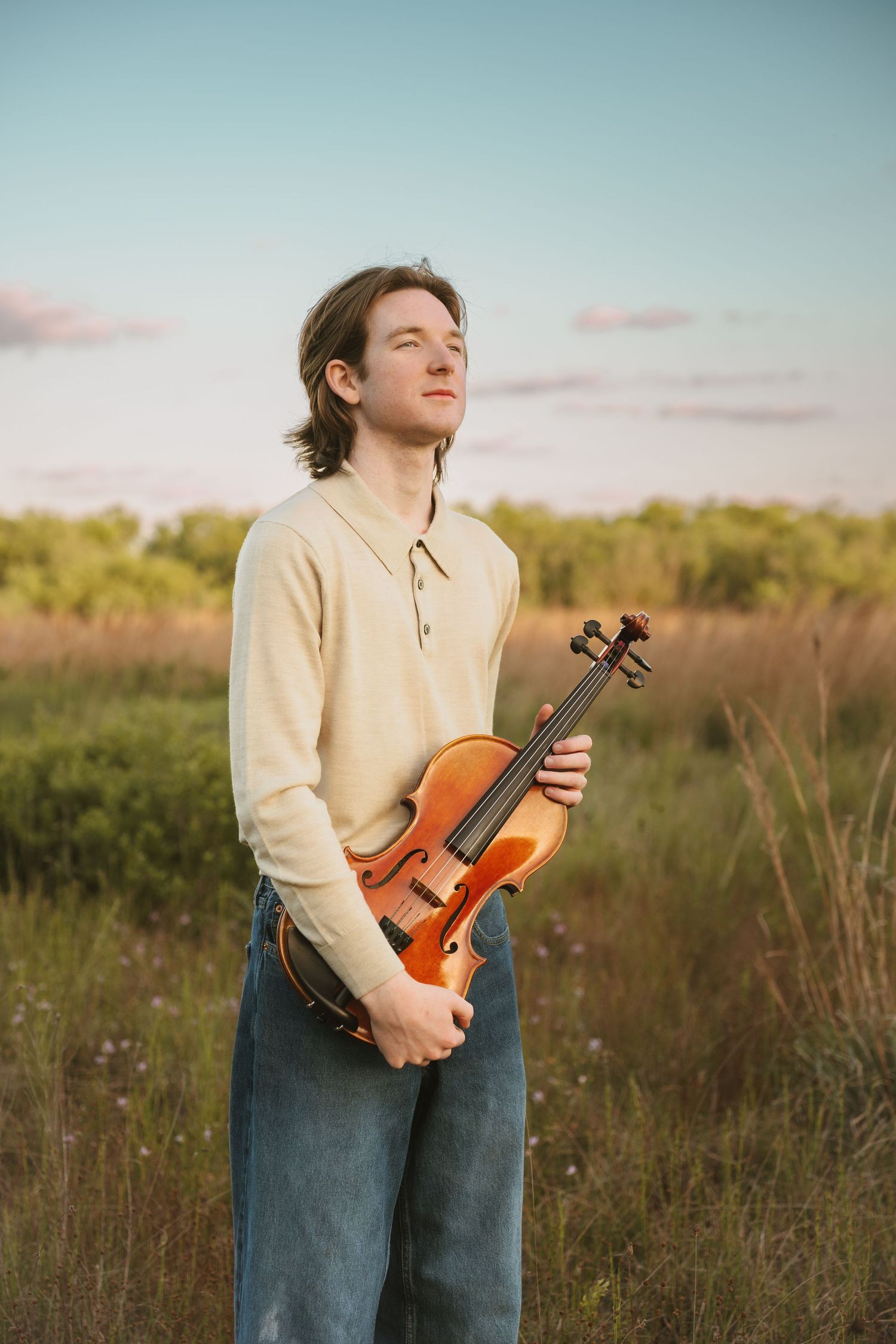 High school graduate holding his violin at sunset during portrait session at Lake Runnymede Conservation Area St Cloud Florida