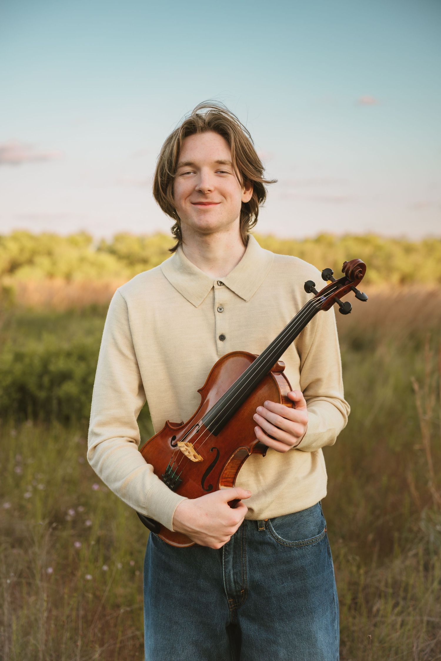High school graduate holding his violin at sunset during portrait session at Lake Runnymede Conservation Area St Cloud Florida