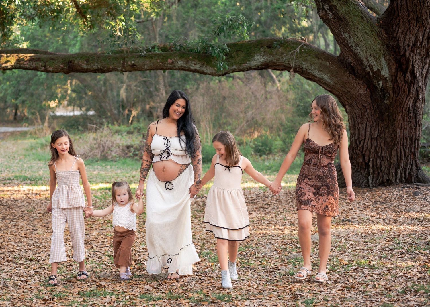 Expecting mother holding hands with her daughters while walking through the oak trees at Lake Runnymede Conservation Area in St Cloud Fl