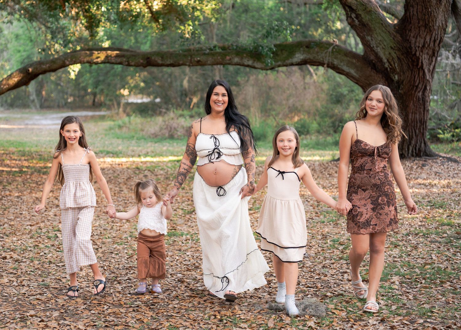 Expecting mother holding hands with her daughters while walking through the oak trees at Lake Runnymede Conservation Area in St Cloud Fl