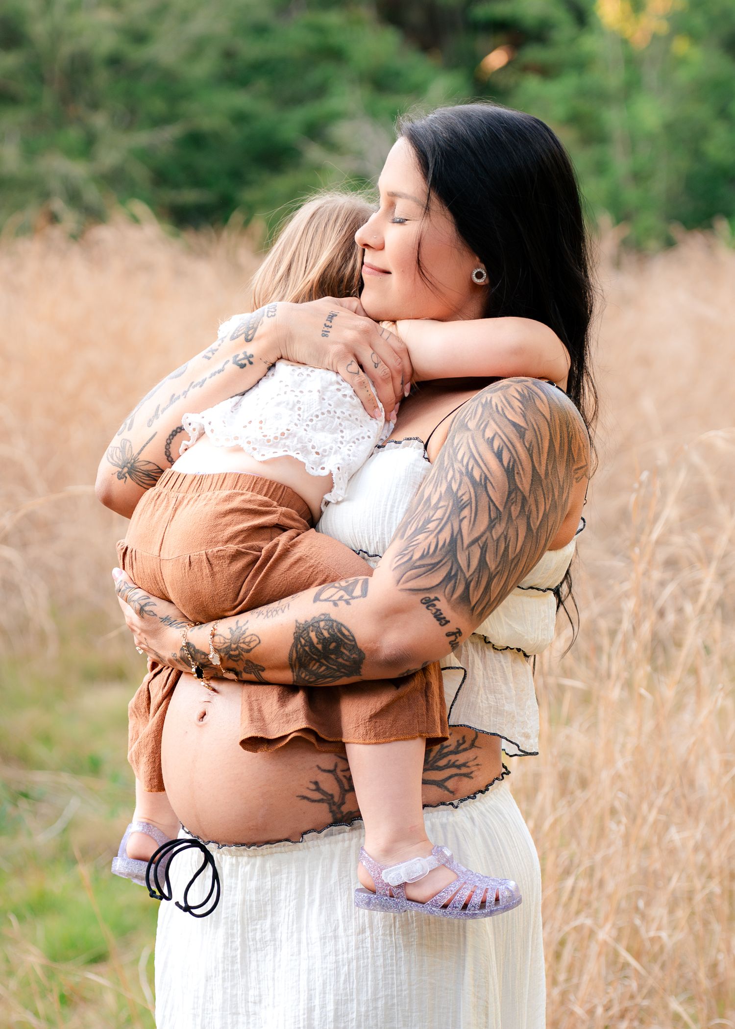 Expecting mother holding daughter during maternity session in the golden grass of Lake Runnymede Conservation Area in St Cloud Florida
