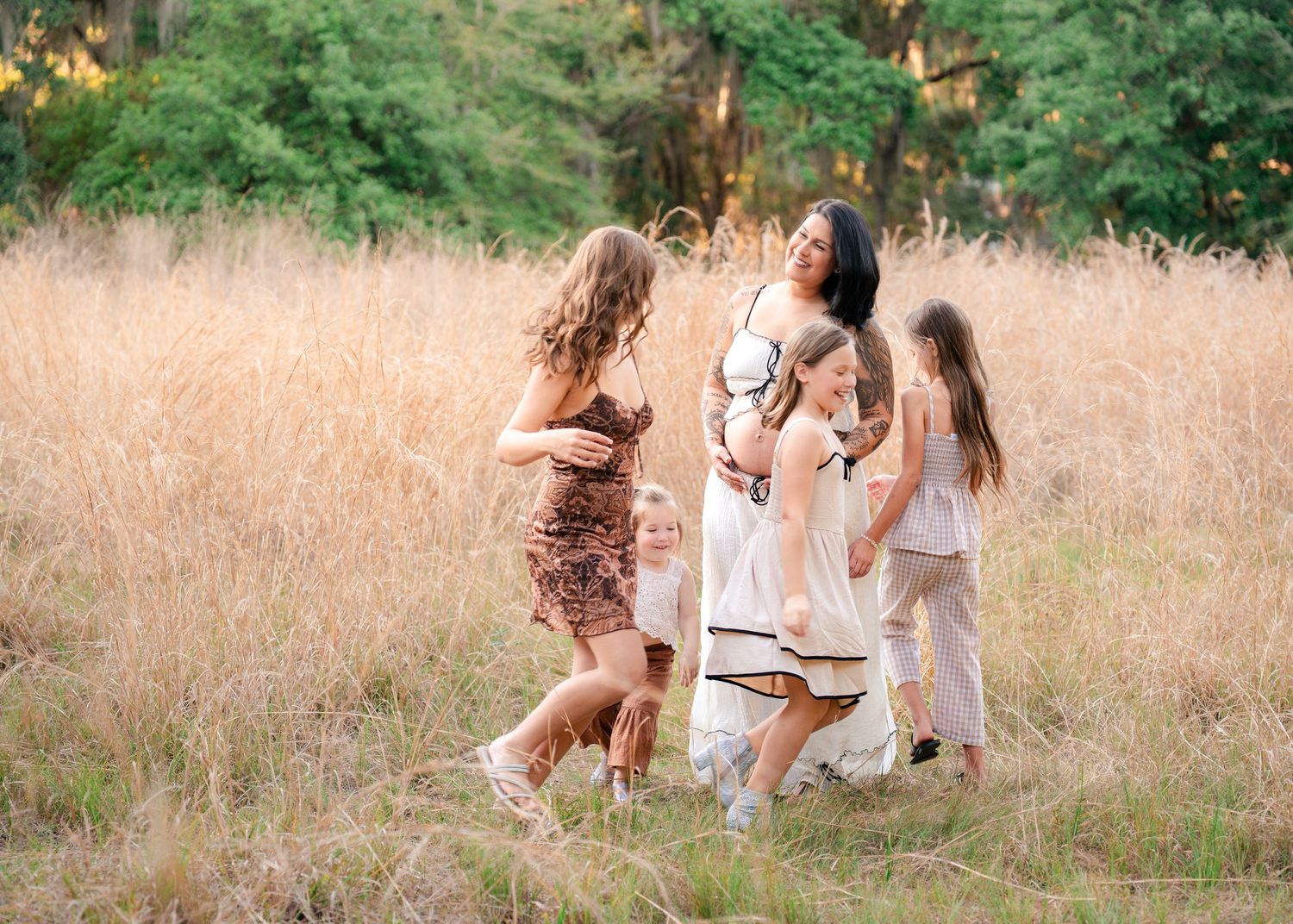 Mother laughing as her daughters run around her in the open fields of Lake Runnymede Conservation Area during maternity session St Cloud FL