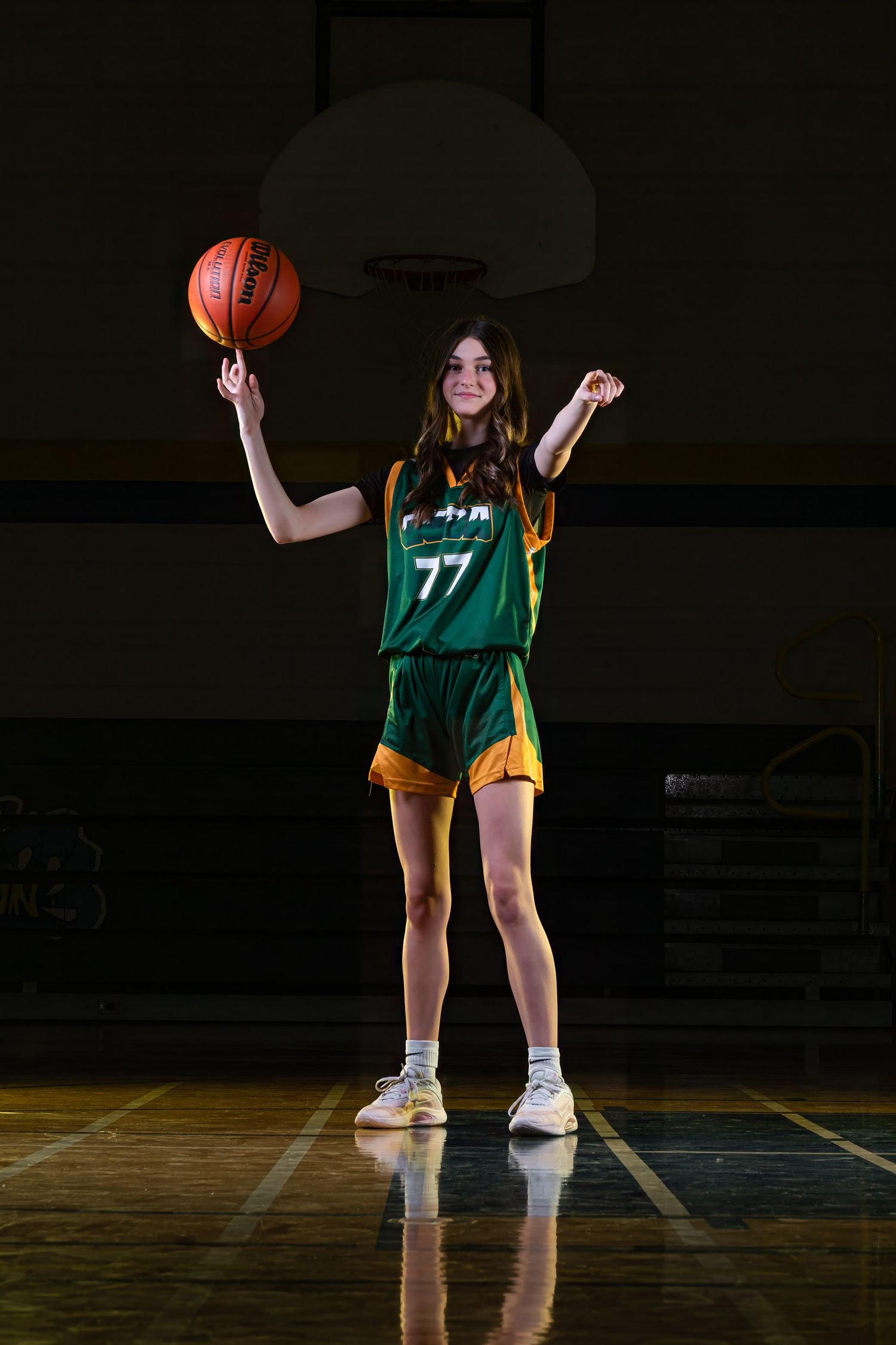 High-end youth sports photography portrait of a girls basketball player number 77 spinning a ball and pointing directly at the camera.