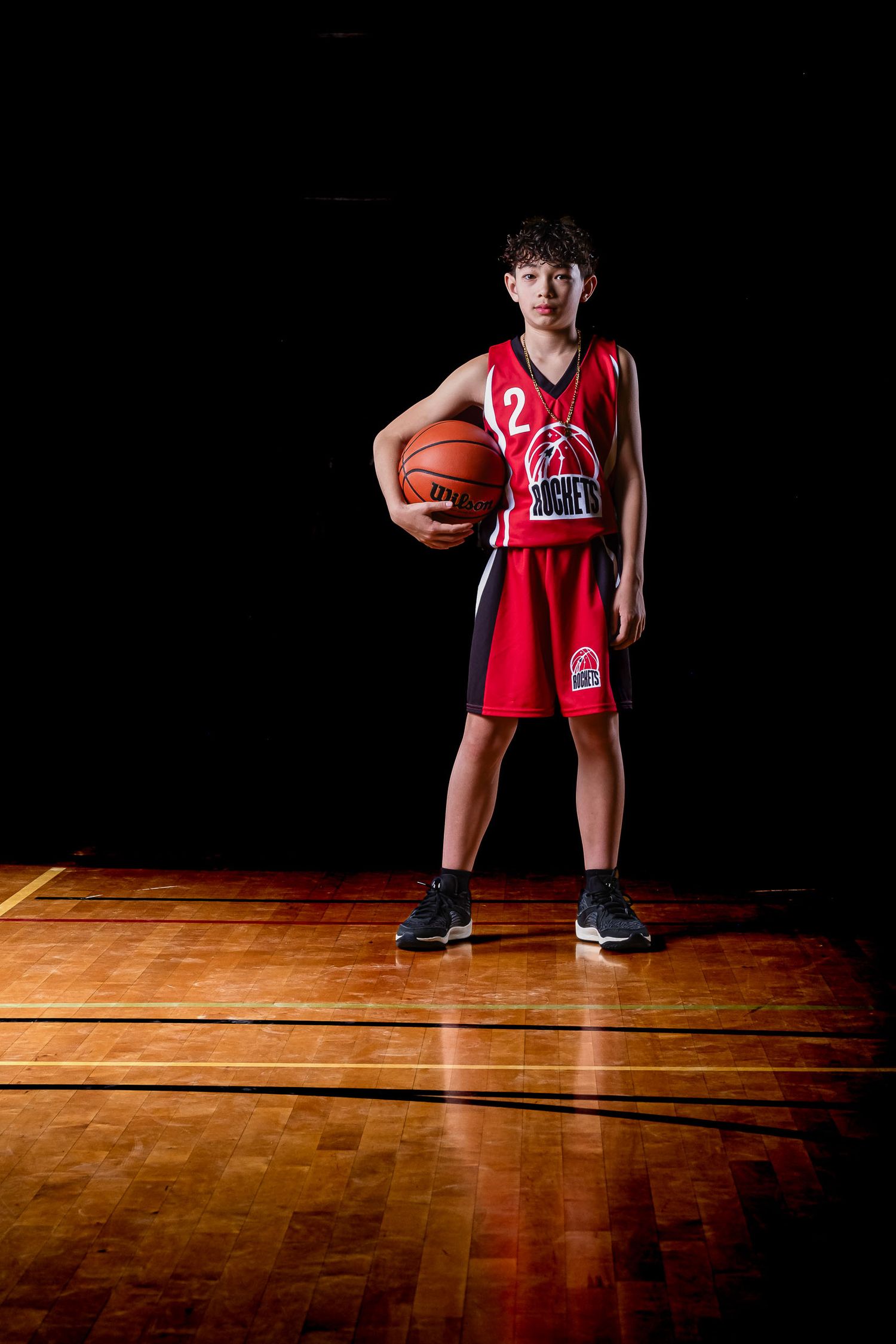 sports photography media day feature showing a moody, cinematic portrait of a basketball player under dramatic rim lighting
