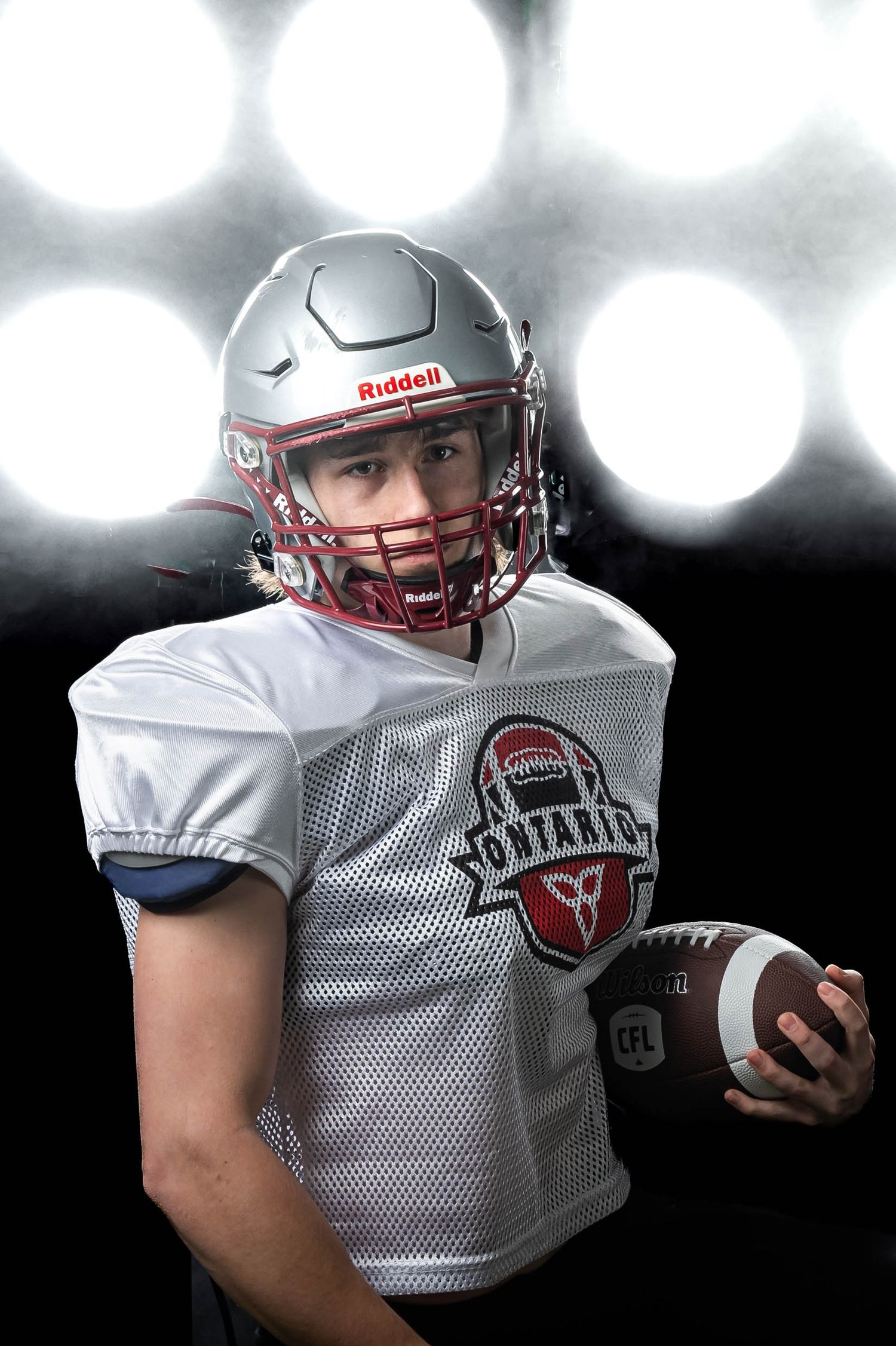 Professional cinematic sports photography of an Ottawa football player holding a football under bright arena lighting.