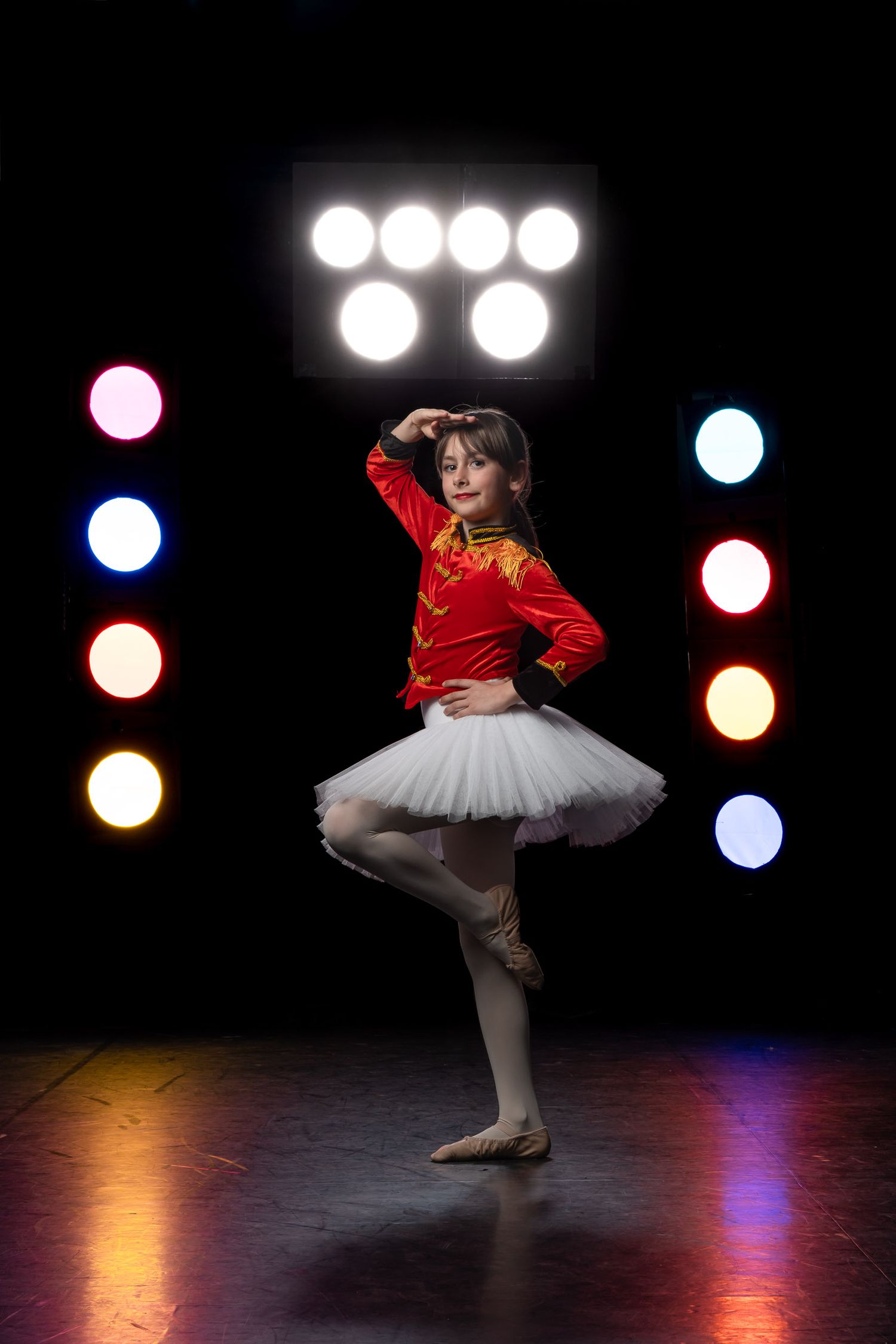 Stunning individual dancer portrait captured mid-pose beneath blazing vertical stage light banks.