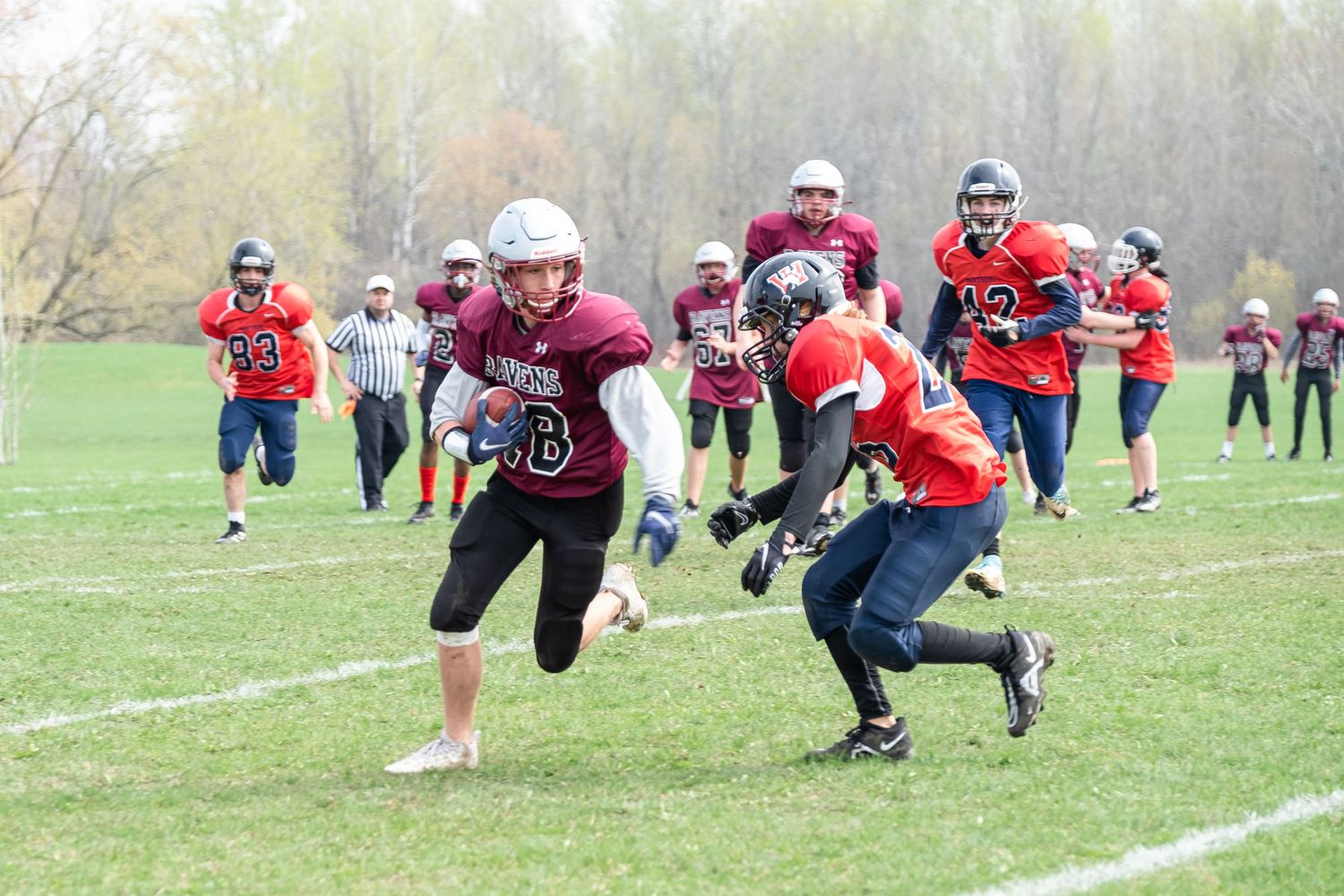 Action shot from an Ottawa youth football game with players in red uniforms sprinting down a green field during play.