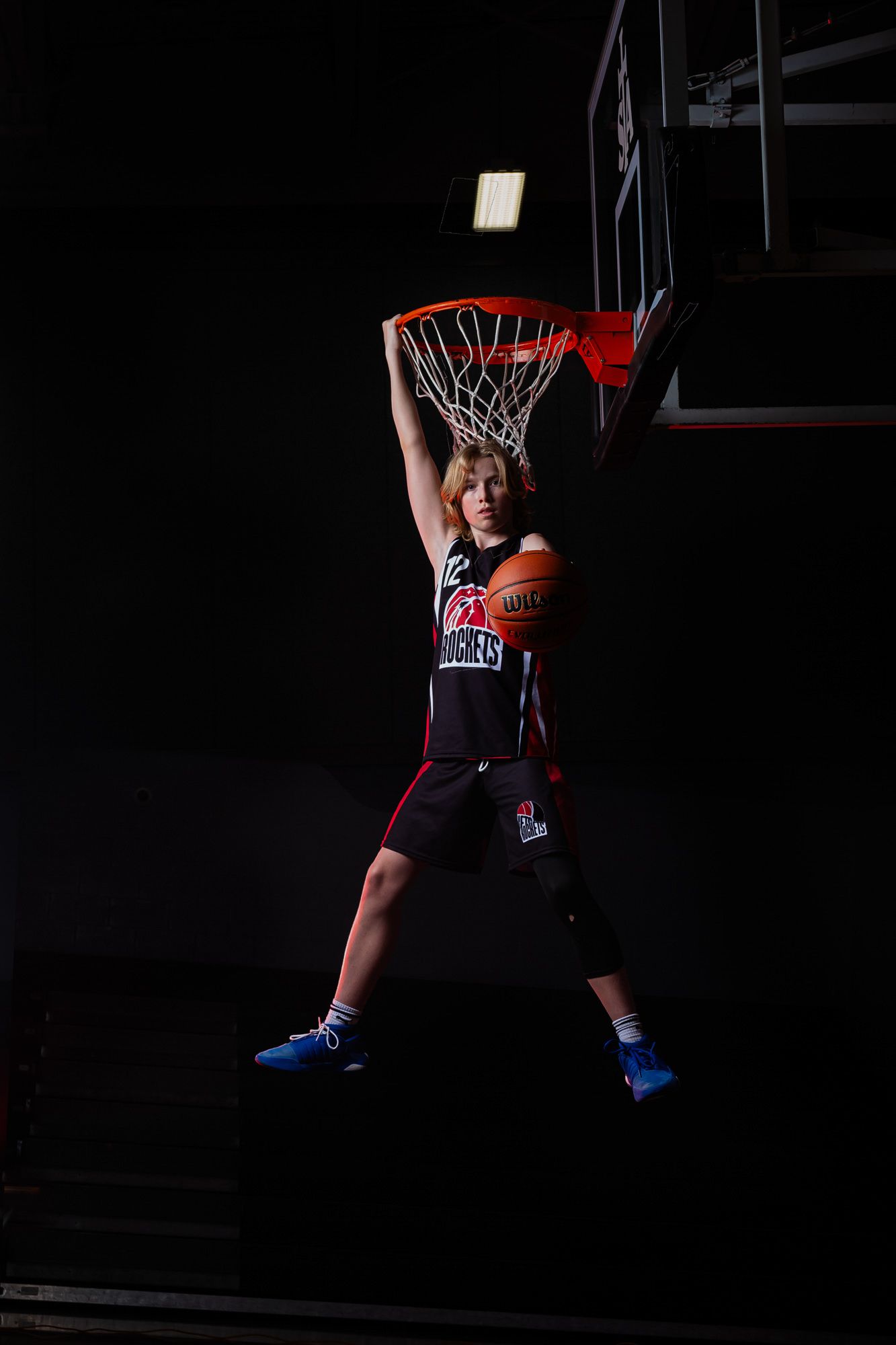 Cinematic on-court basketball portrait with player hanging from net by one arm by The Show Sports Media in Russell, Ontario.