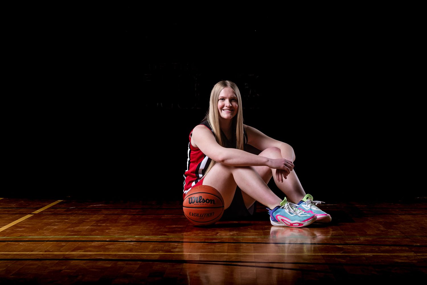 Basketball portrait of an athlete using dramatic studio lighting sitting on the court smiling