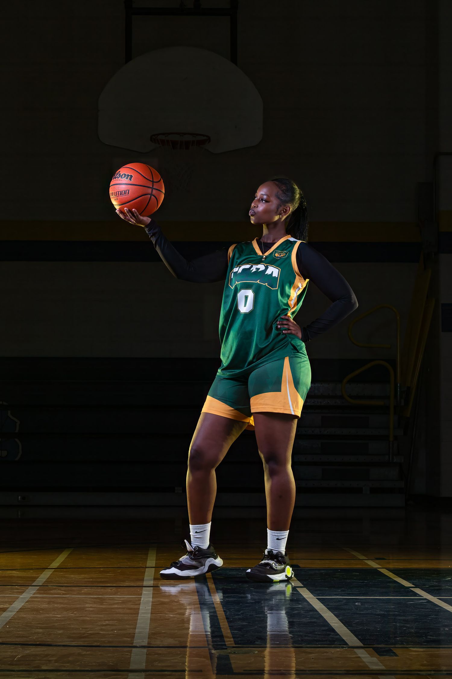 Dramatic sports portrait photography of a female basketball player wearing number 0 posing in profile while balancing a basketball on a dar