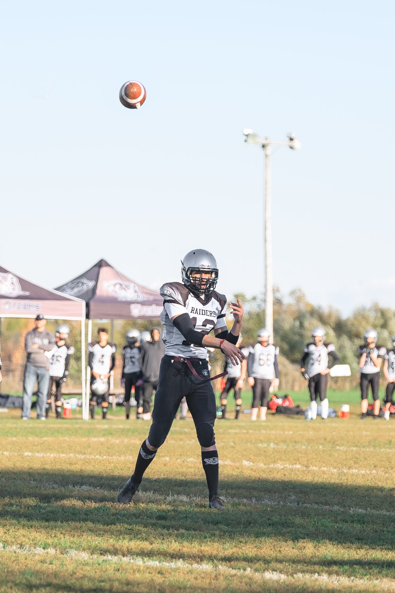Ottawa football photography capturing a player throwing a football high into the bright blue sky during a sunny day game.