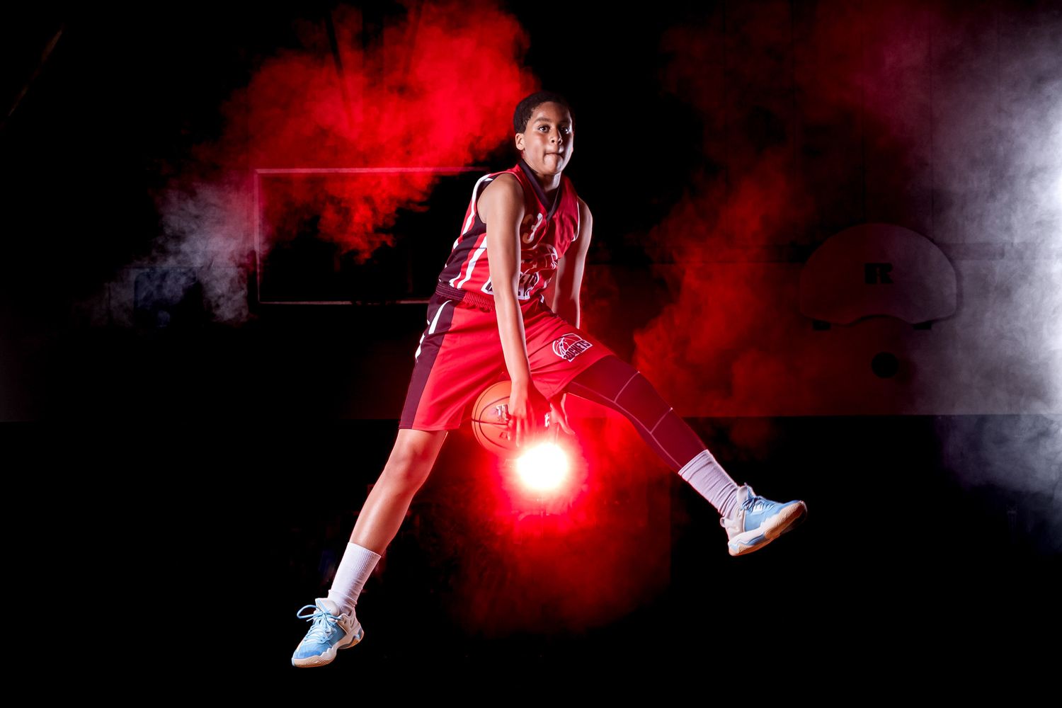 Young basketball player jumps in the air with ball in cinematic basketball action portrait using dramatic studio lighting and effects