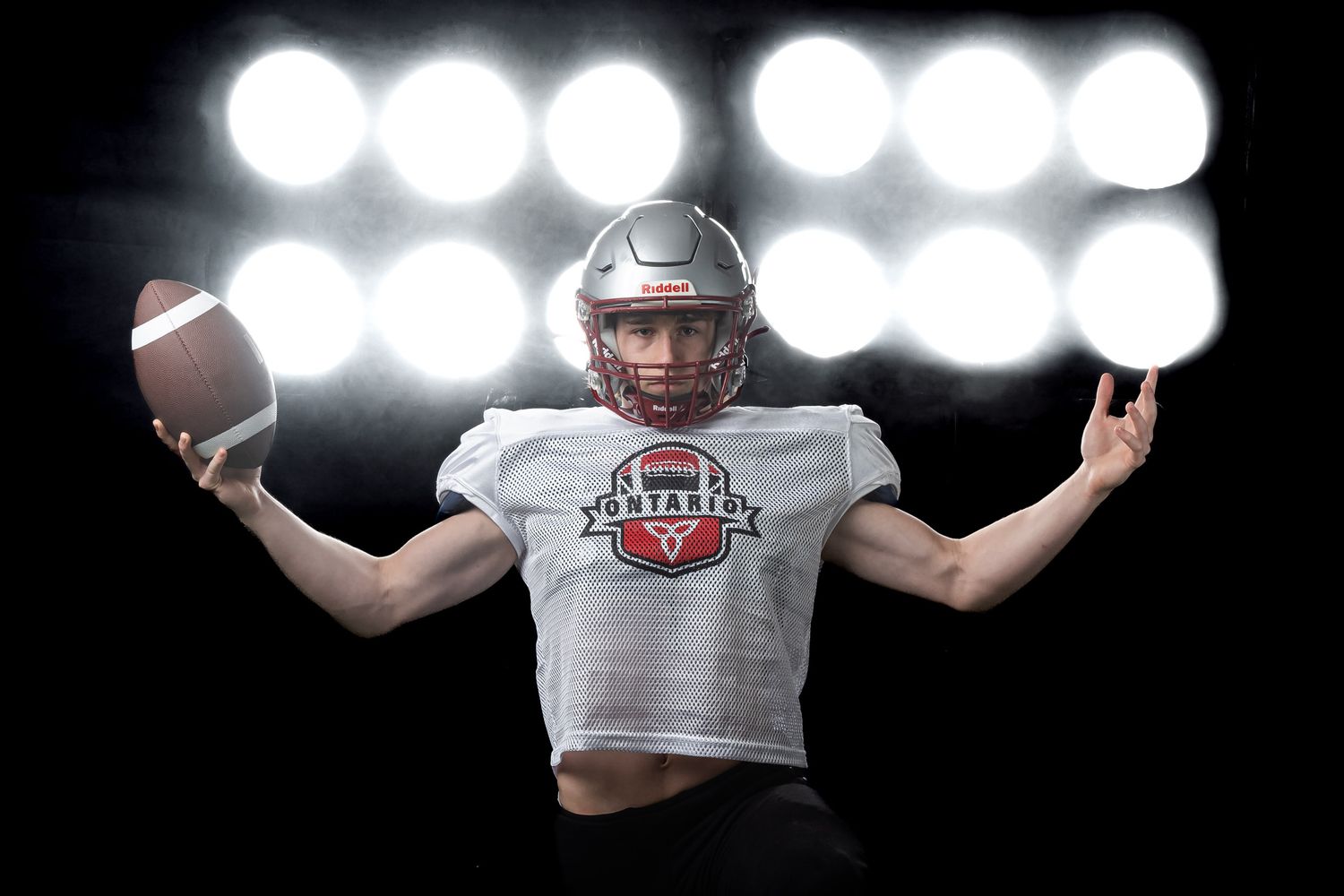 Ontario youth football photography featuring an elite player holding a football out against bright lights.