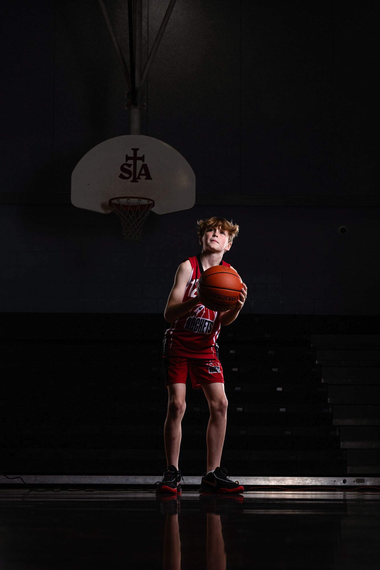 Cinematic basketball action portrait using dramatic studio lighting and effects of a young boy about to take a shot at the net