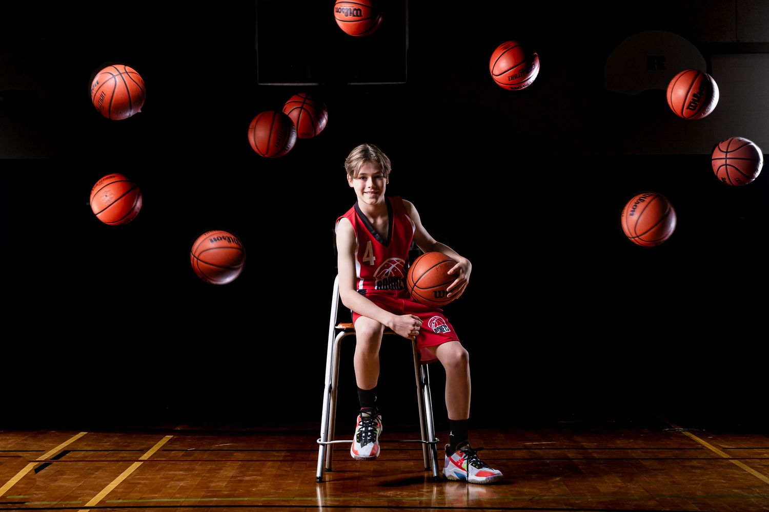 Cinematic on-court basketball portrait with player sitting down and basketballs being thrown behind in Eastern Ontario