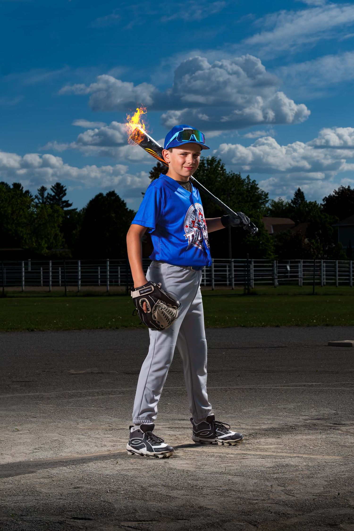 Young boy in baseball uniform with baseball bat over his shoulder. There is fire coming off the baseball bat