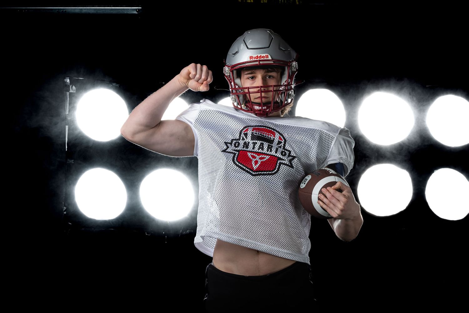High-end football media day portrait of an athlete flexing under bright, dramatic stadium rim lighting