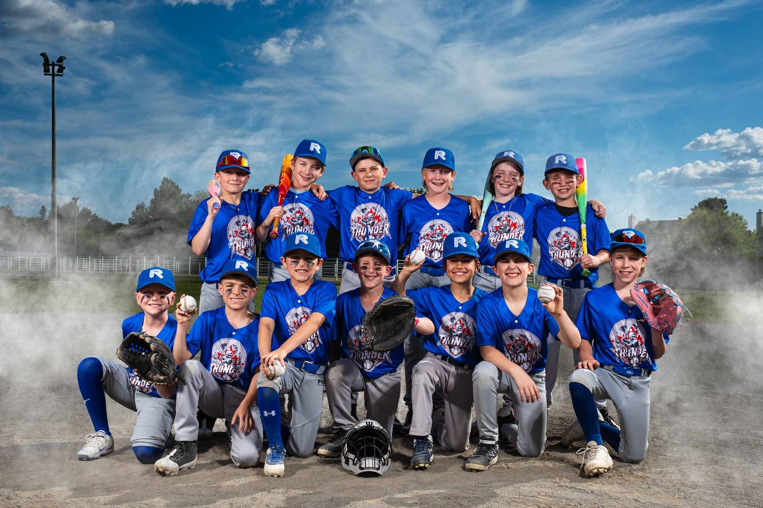 Team of baseball players posing some have bats some have balls and gloves. Surrounded by fog and smiling for the photographer