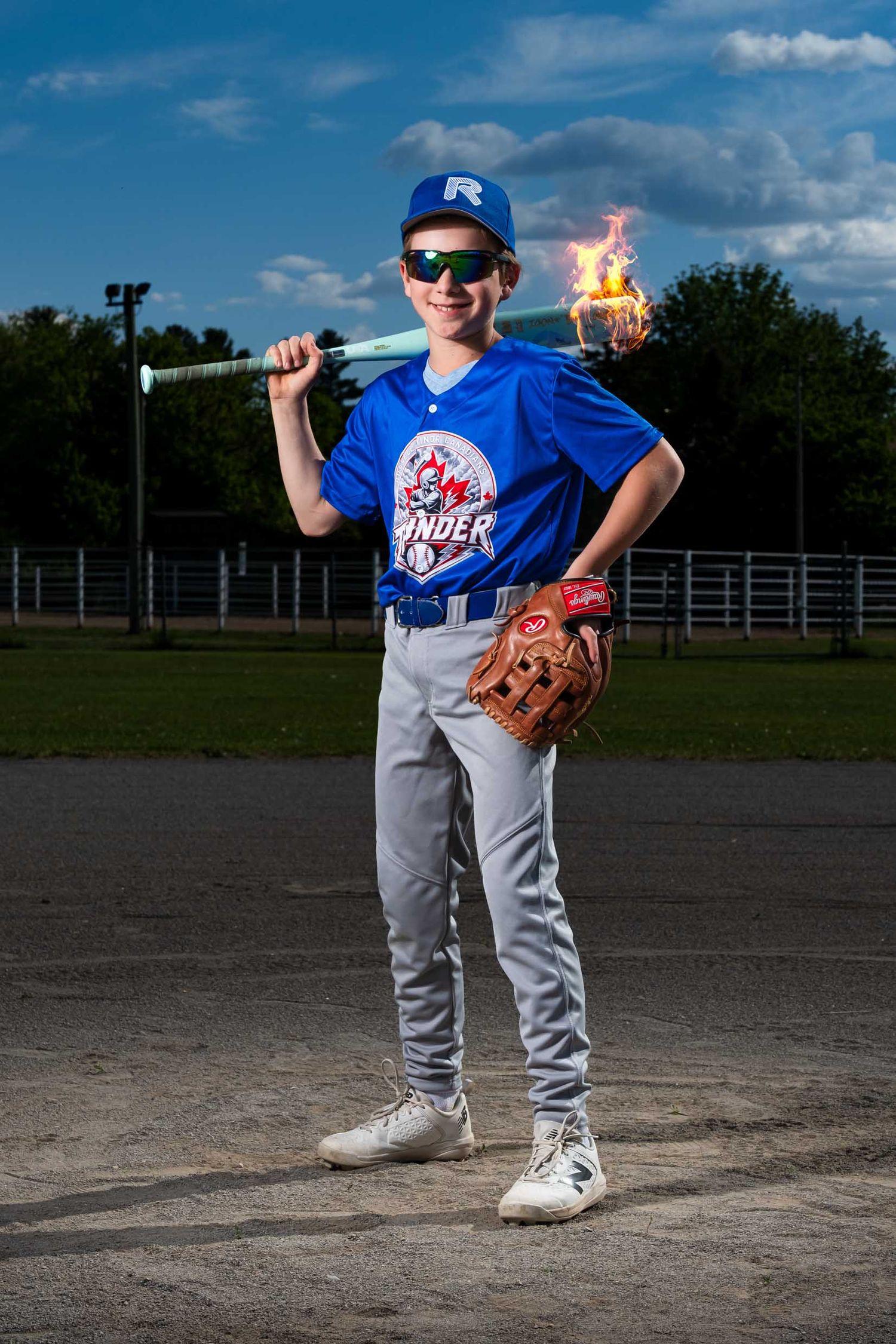 Young boy in baseball uniform on the diamond with bat over his shoulder. There is fire coming off the baseball bat