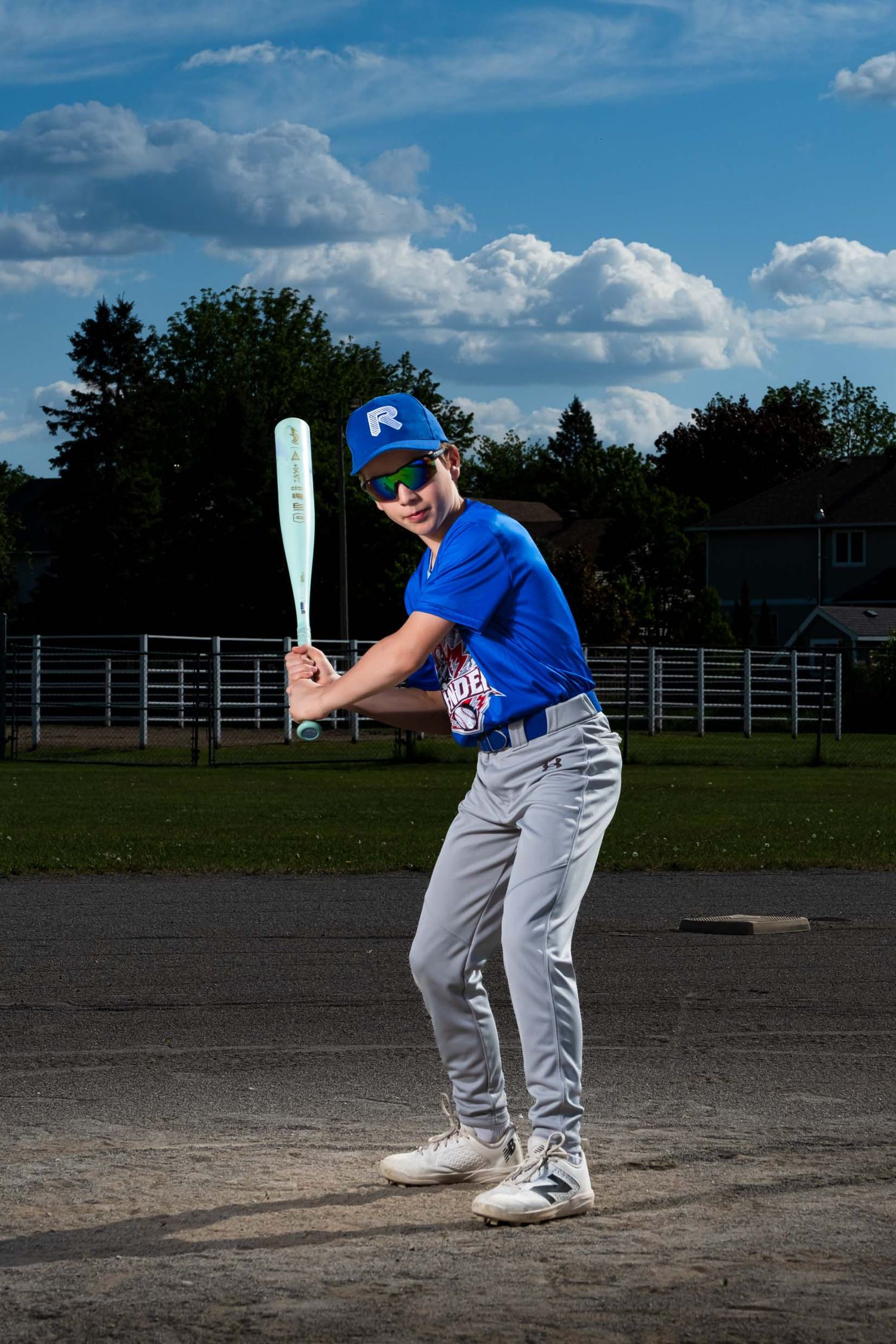 Baseball player swinging for the ball in a pose looking forward with hat and sunglasses on