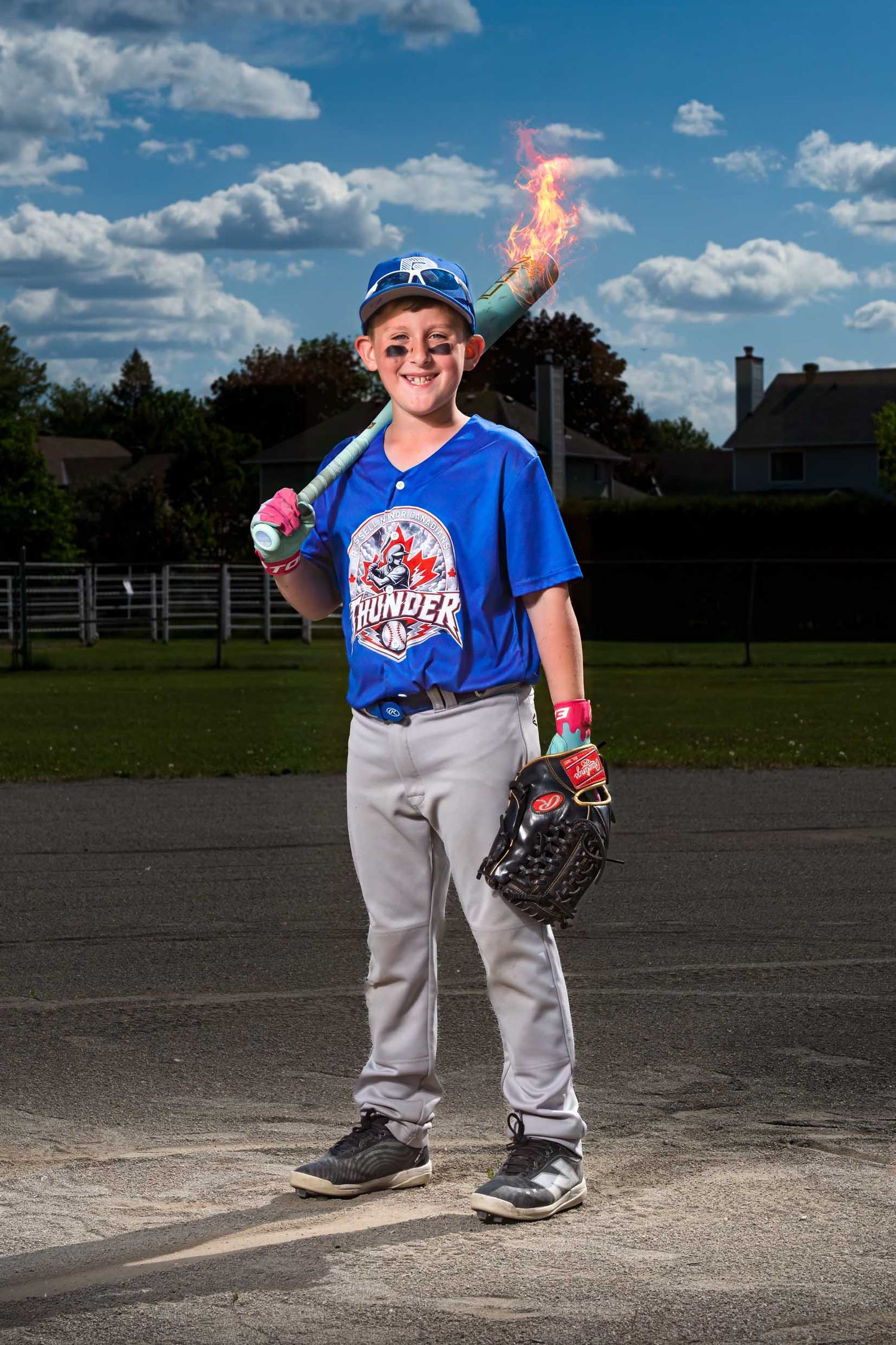 Young boy in baseball uniform with baseball bat over his shoulder. There is fire coming off the baseball bat