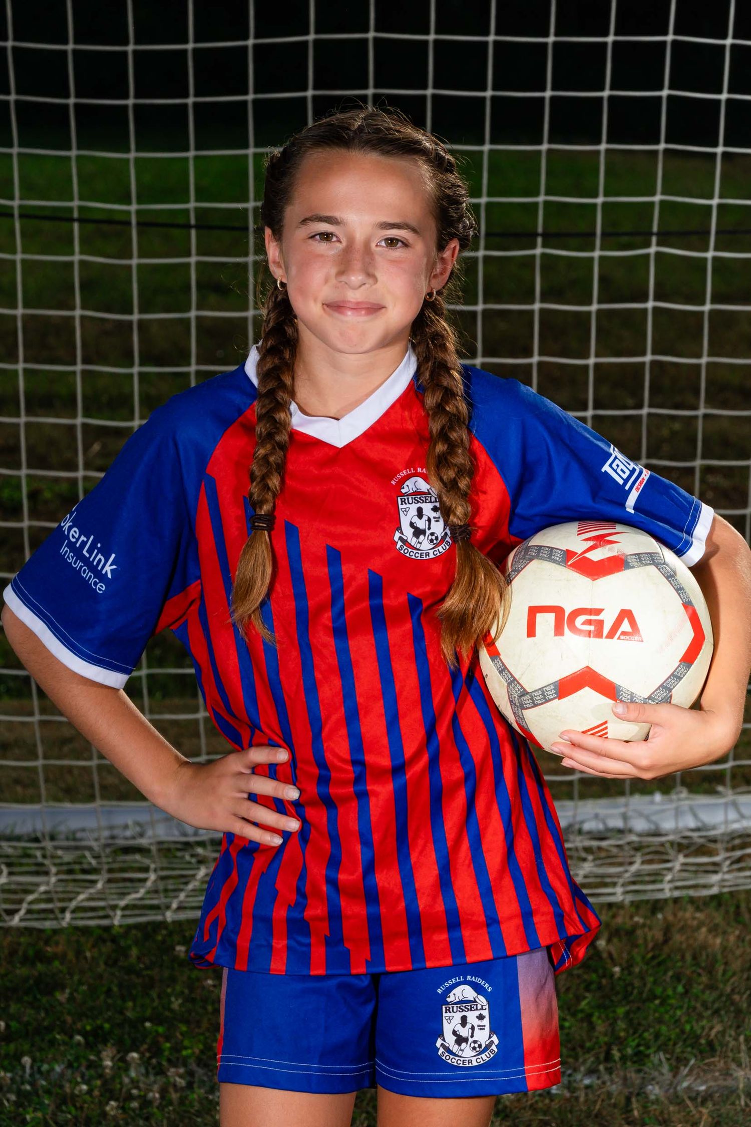 Close-up sports portrait of a young soccer player in a blue and red uniform holding a ball under dramatic studio lights.