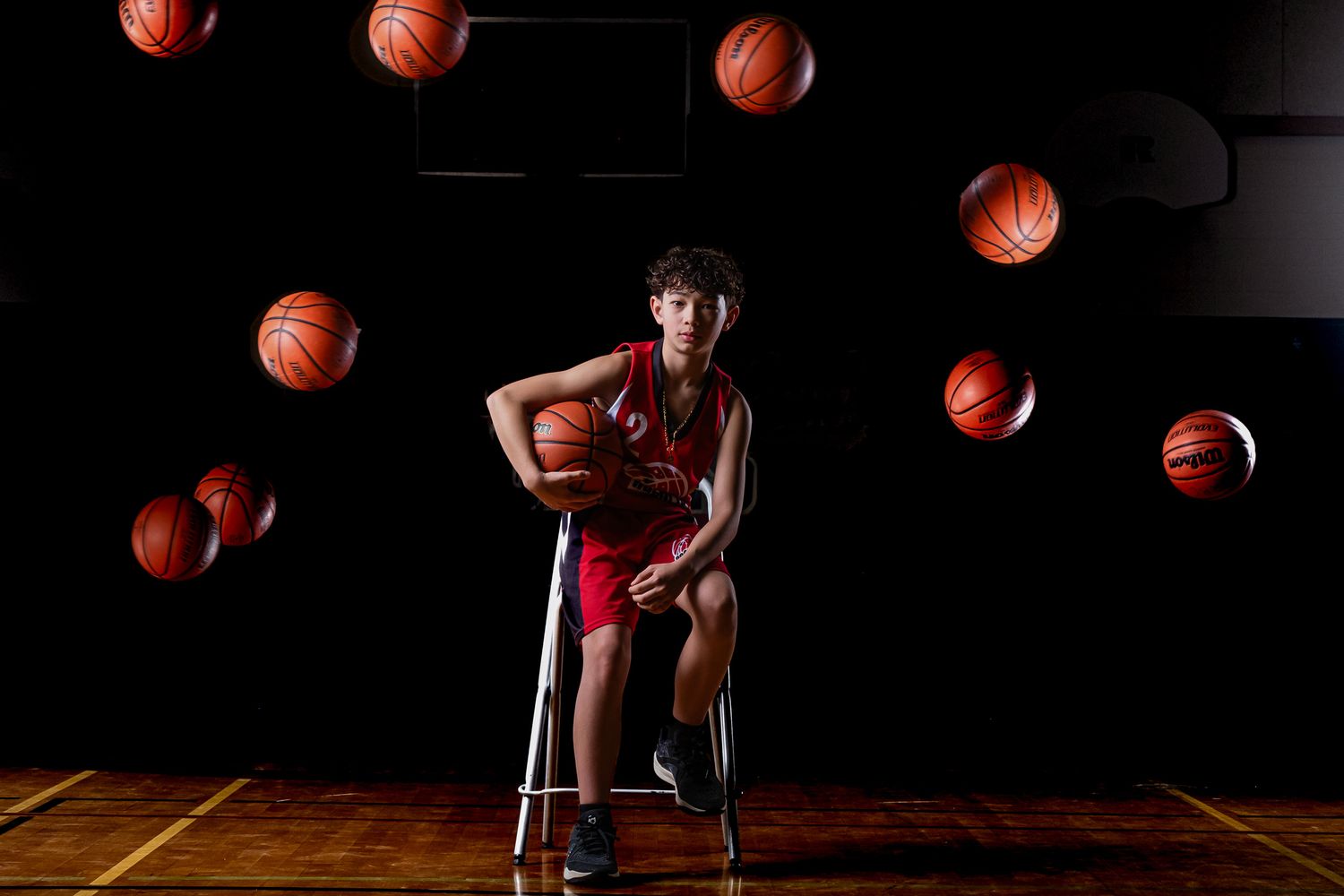 Stylized basketball portrait of stoic athlete seated, basketballs in motion overhead, technical composite photography,