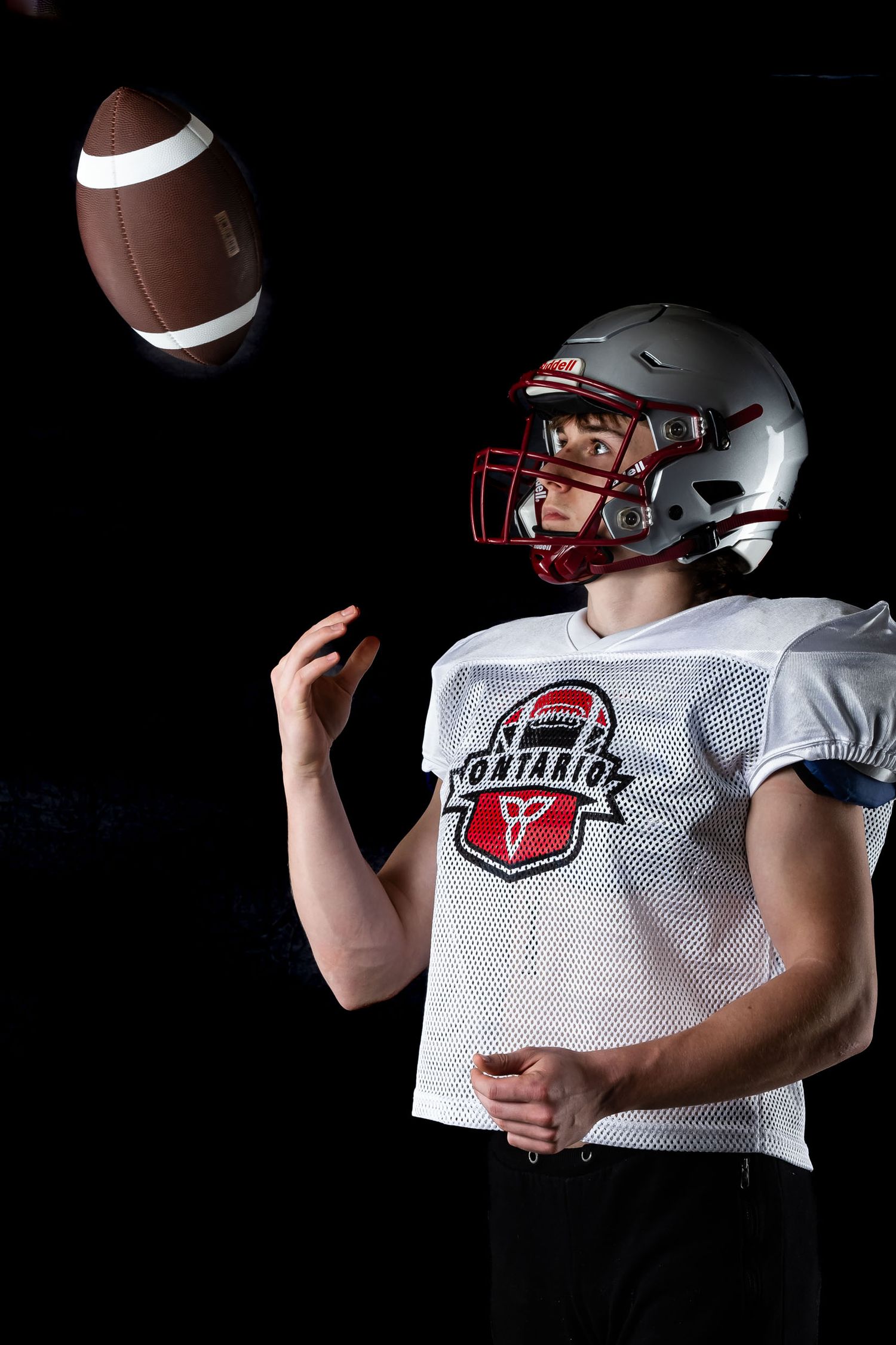 Cinematic sports portrait of an Ottawa youth football player tossing a football under dramatic studio lighting.
