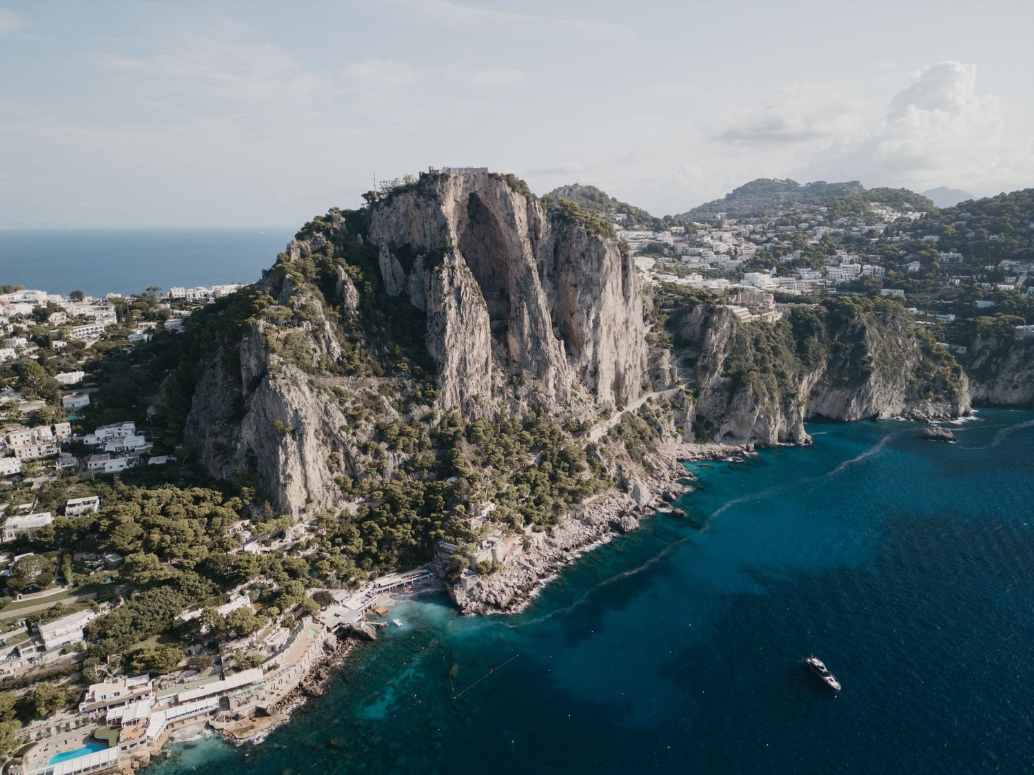 Aerial panoramic view of the rugged coastline and blue waters of Capri Island in Italy with dramatic limestone cliffs.
