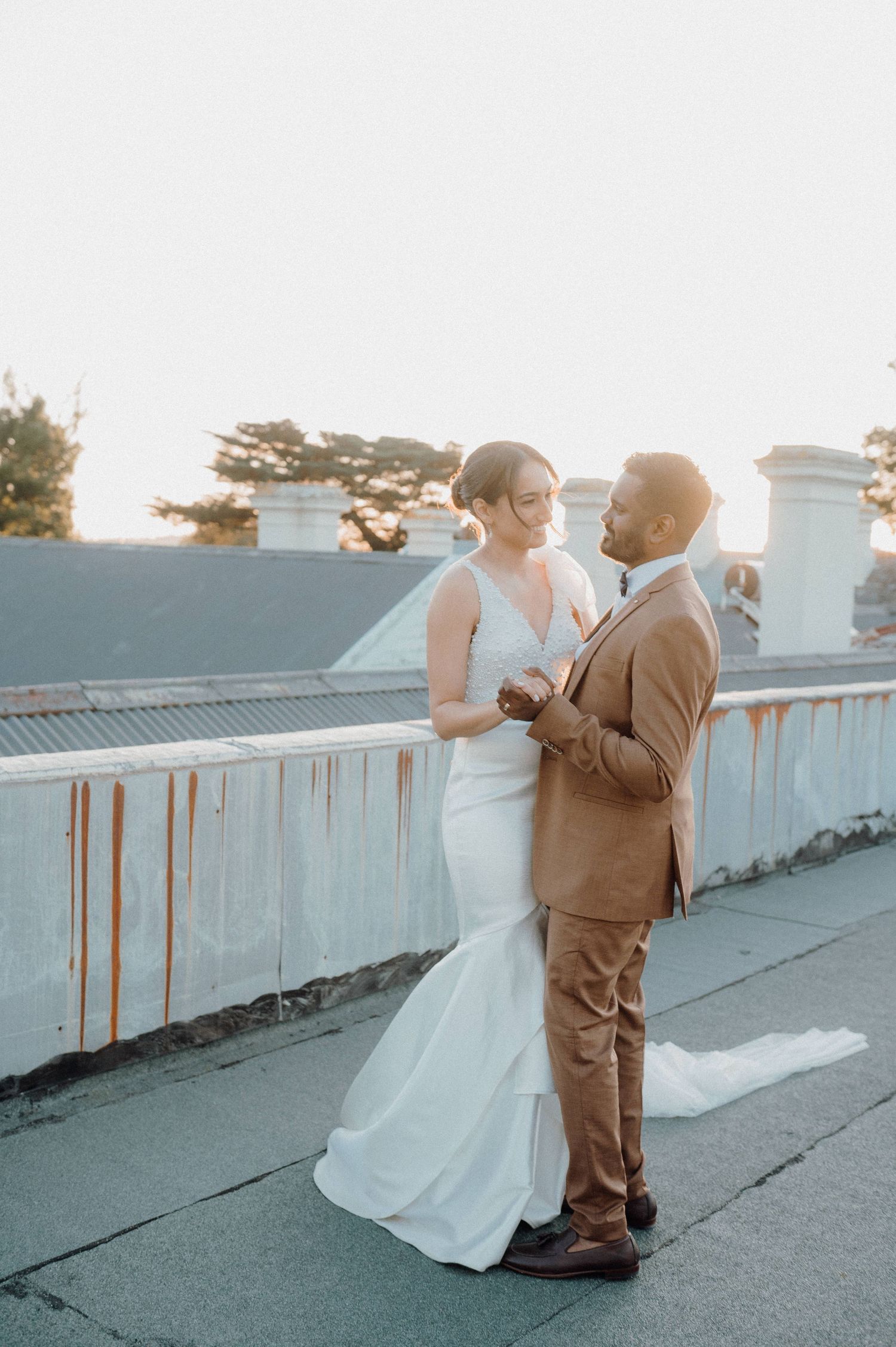 Elegant couple in wedding attire sharing a moment on a balcony at sunset.