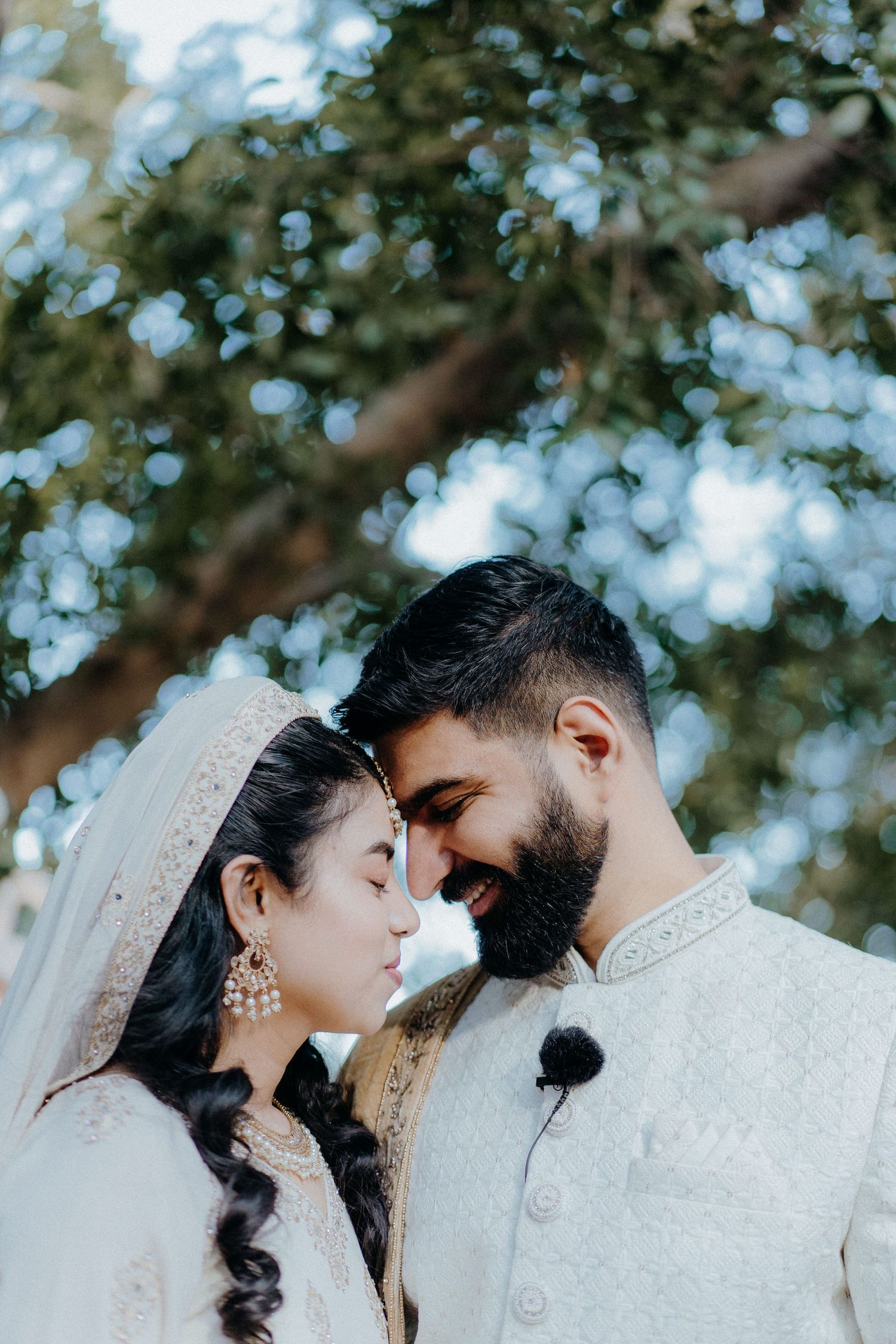 Intimate wedding portrait outdoors with soft bokeh tree lighting.