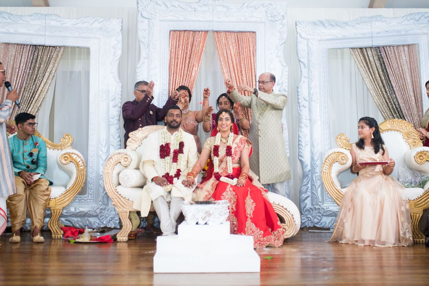Traditional Indian wedding ceremony setup with elegant white and gold decor and coral drapes in an indoor venue.