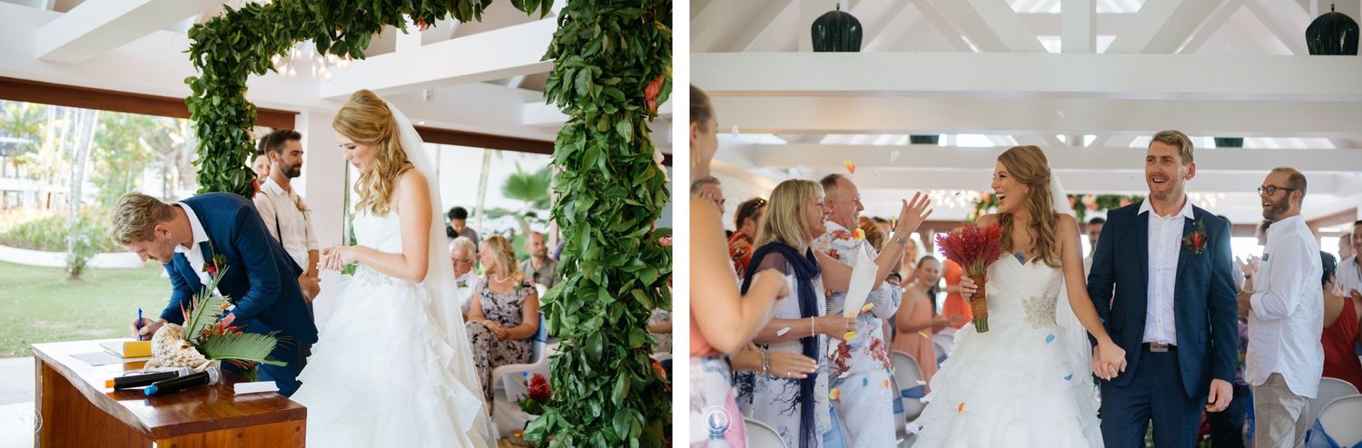 A wedding ceremony in a bright venue decorated with greenery and white accents.