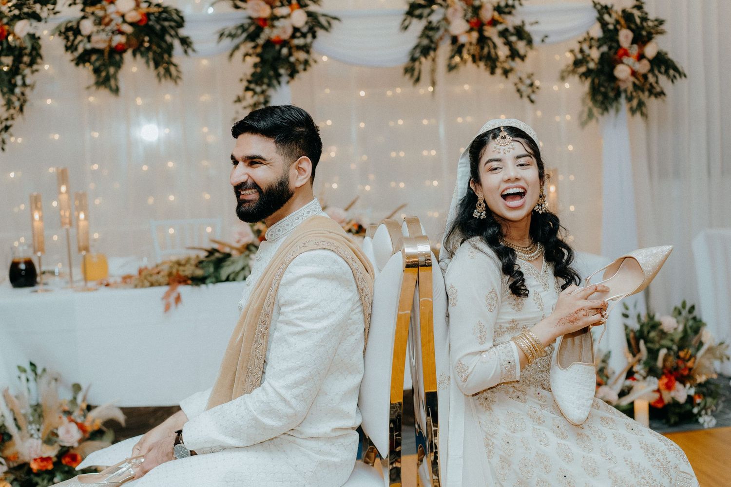 A couple shares a joyful moment at their wedding ceremony with floral decorations and twinkling lights in the background.