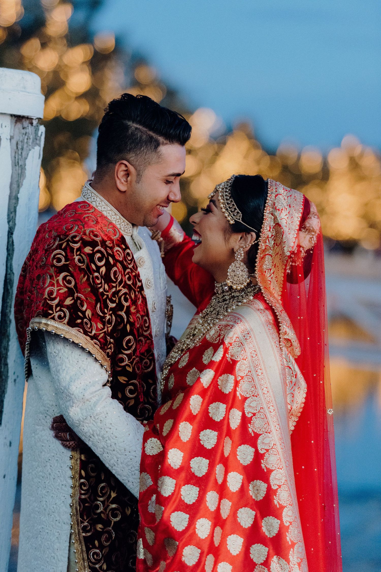 Intimate moment captured of a couple in traditional South Asian wedding attire against bokeh lights.