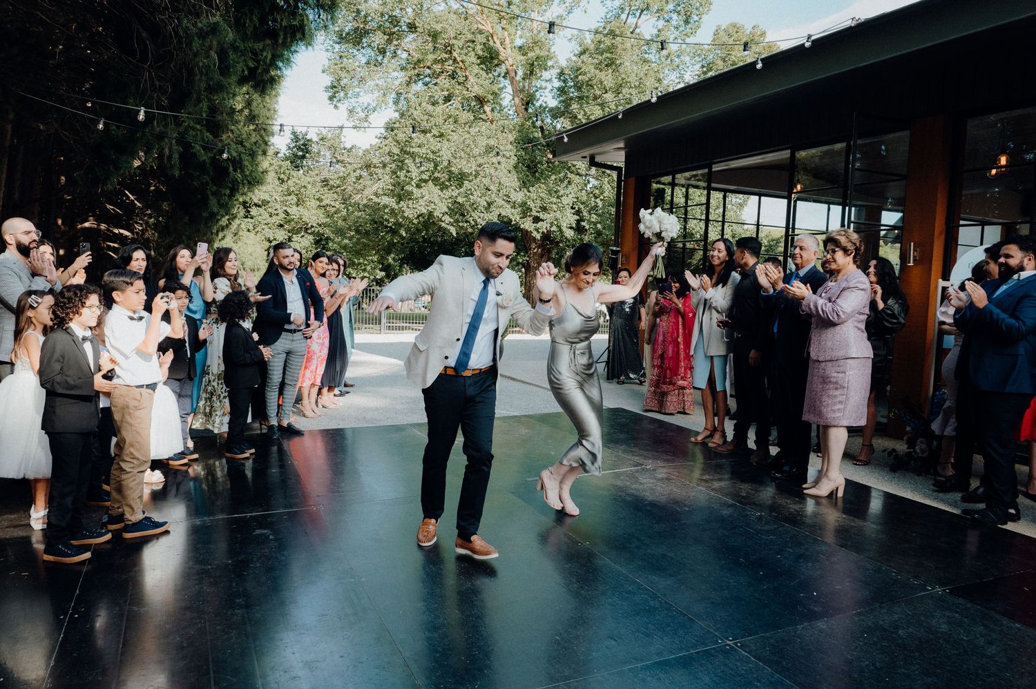 Wedding guests dance and celebrate on outdoor covered patio during reception.