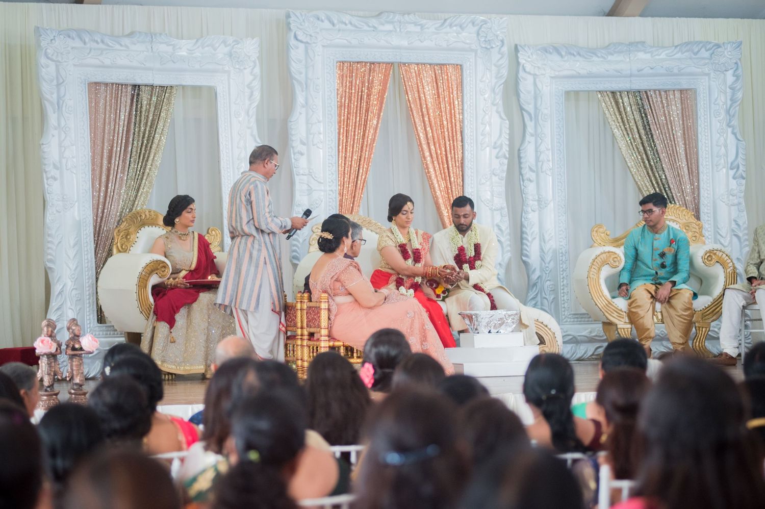 Traditional Indian wedding ceremony with audience watching from decorated venue.