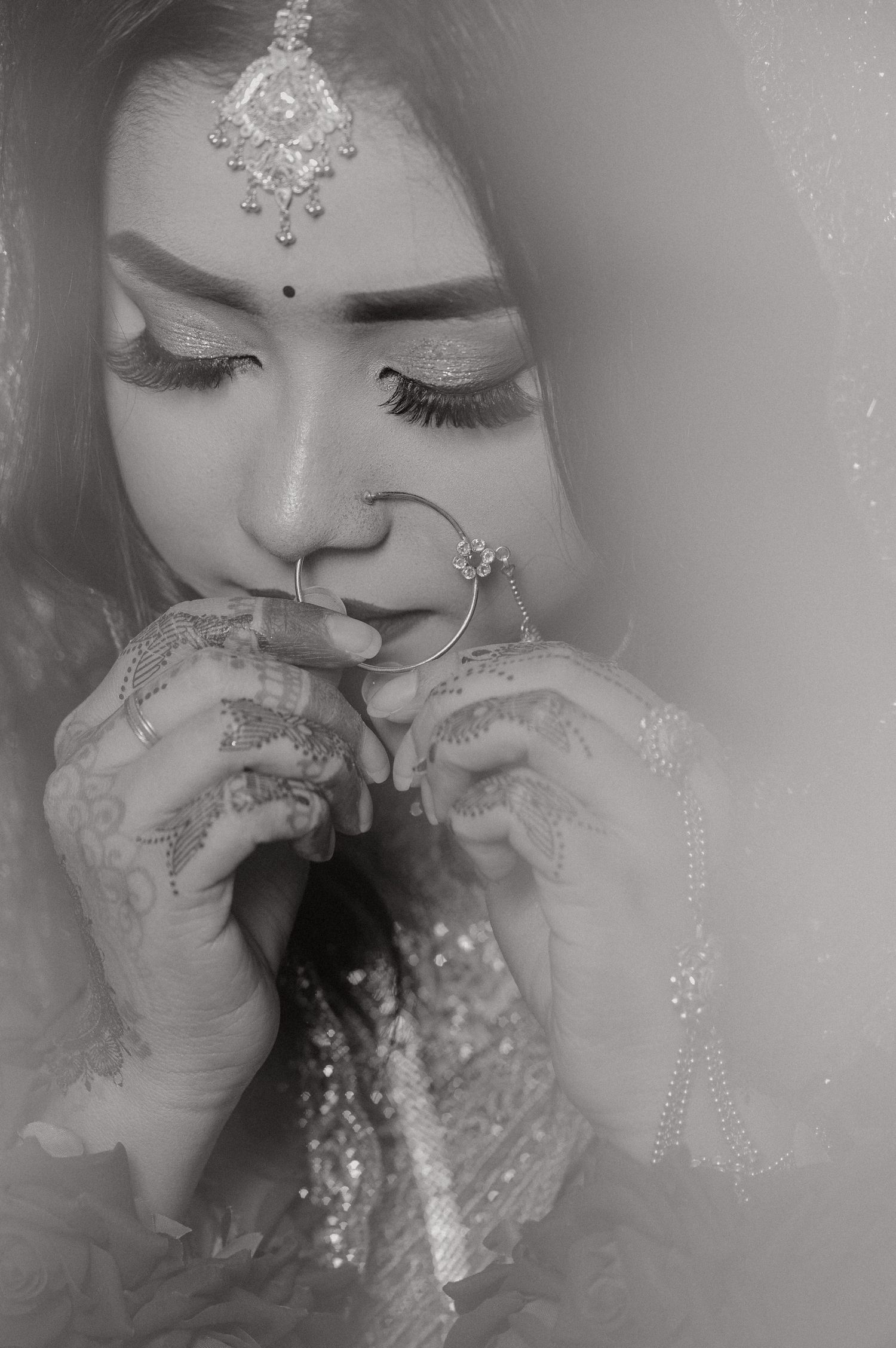 Artistic black and white portrait showing traditional bridal jewelry and henna-decorated hands.
