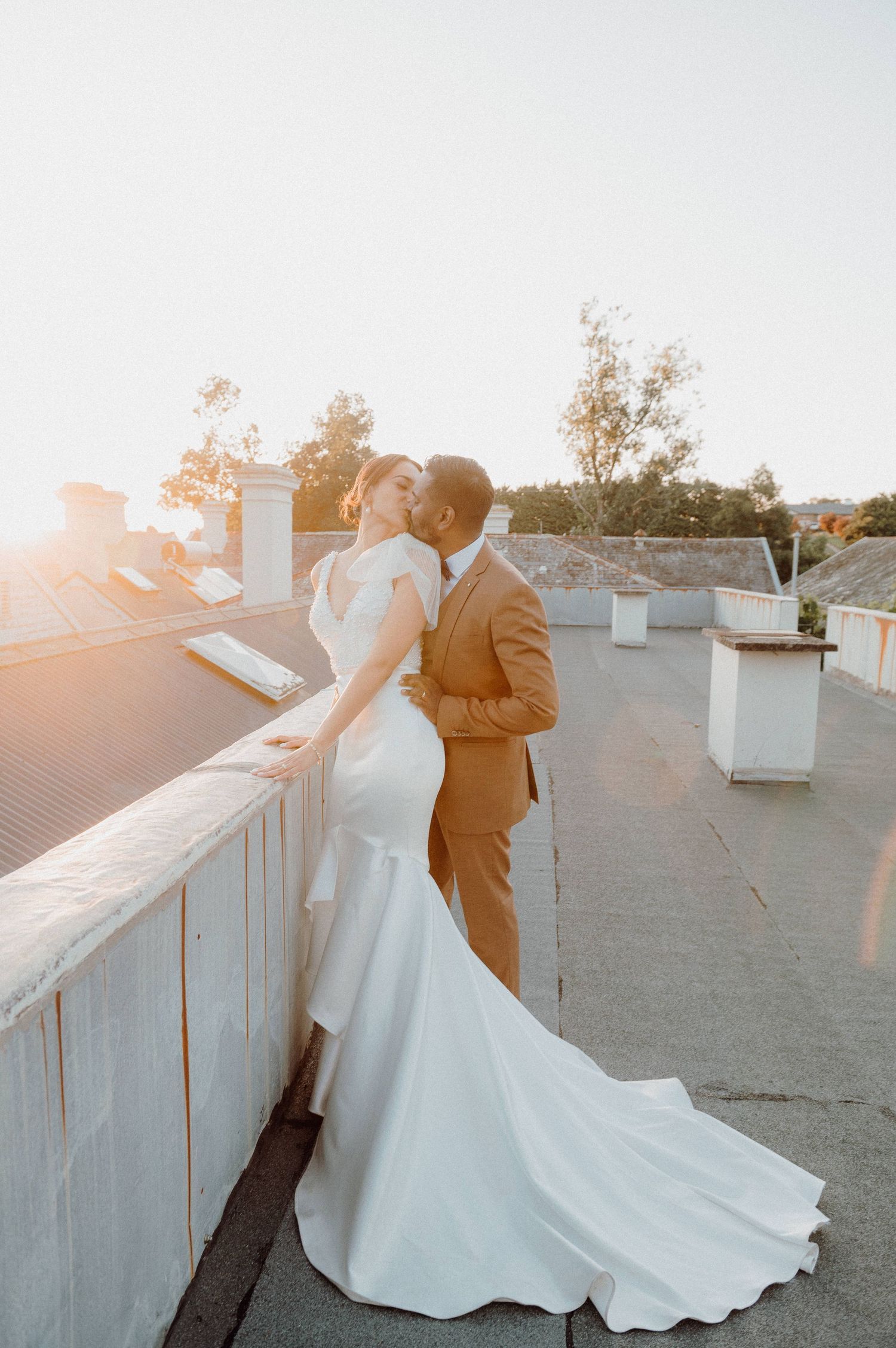 Romantic sunset moment captured of couple in wedding attire on rooftop.