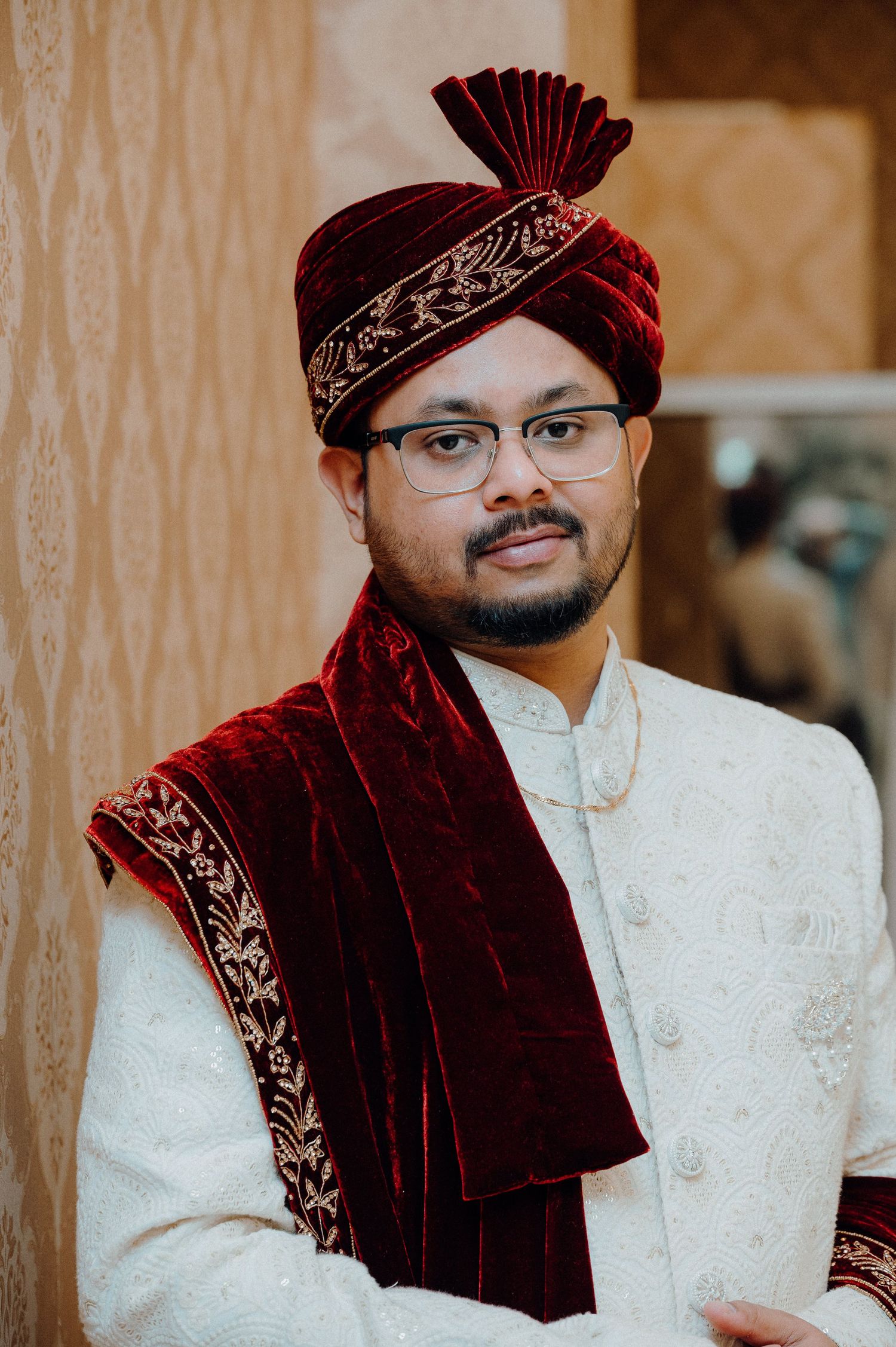 Groom wearing traditional velvet maroon turban and white sherwani smiles at camera.