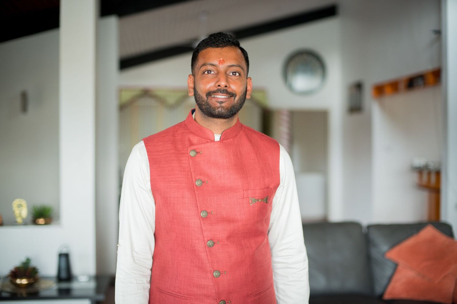 Person wearing coral nehru jacket and white kurta smiling at camera in modern interior.