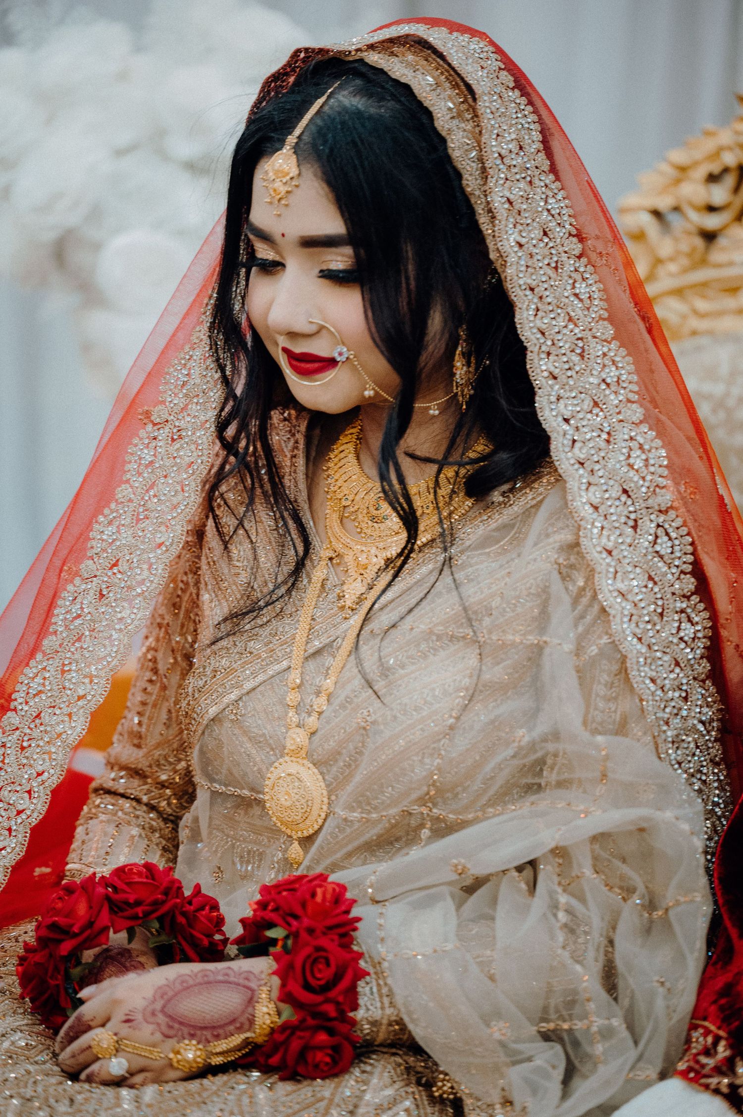 Bride in traditional South Asian attire with intricate embroidery and red veil.