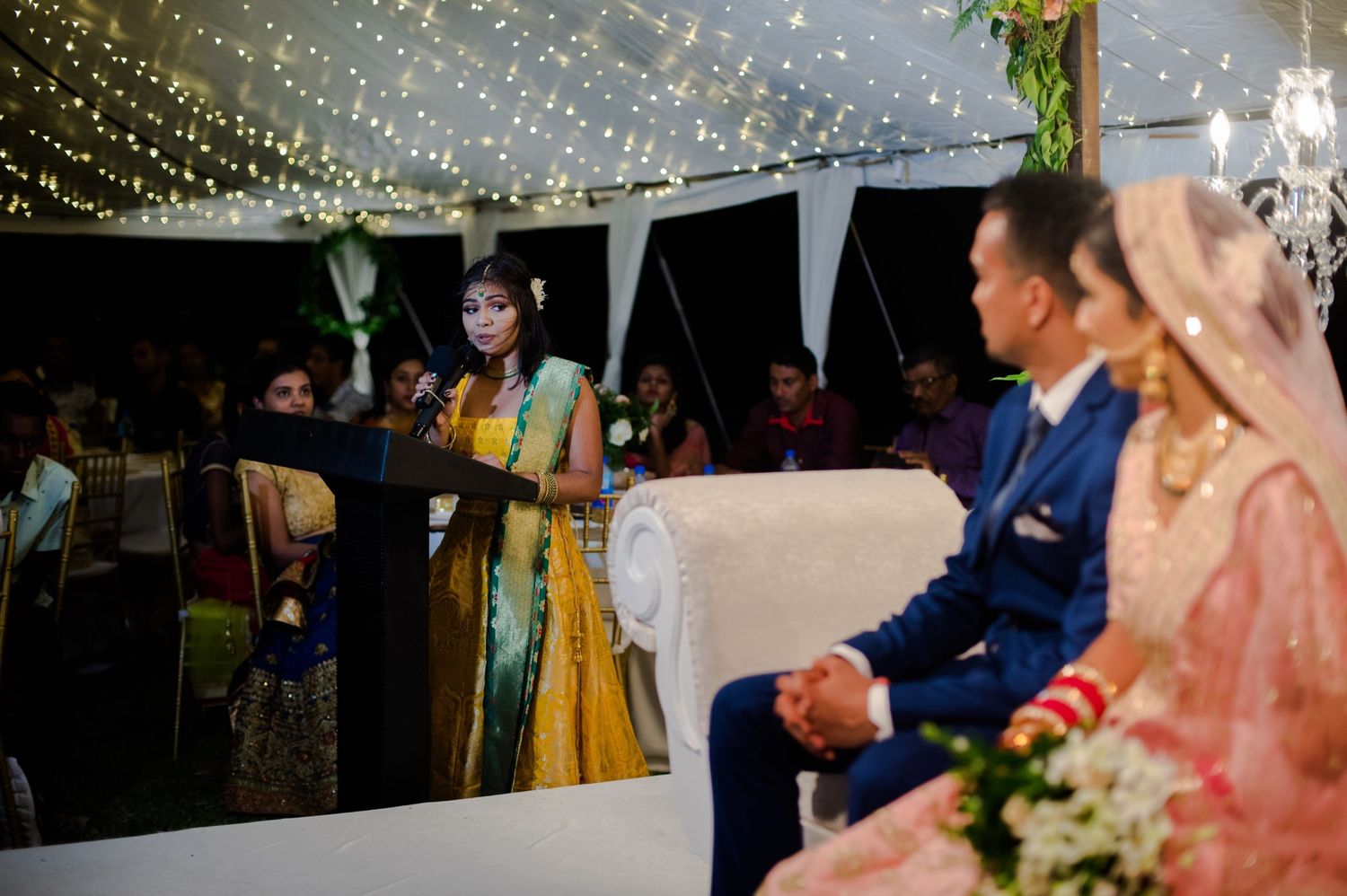 Evening wedding reception scene with guests celebrating under twinkling lights.