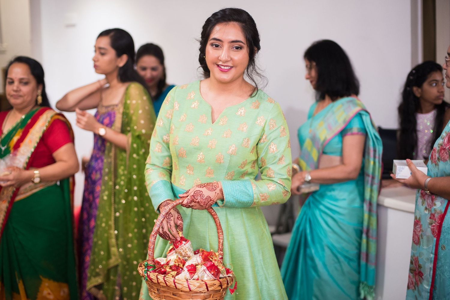 A woman in mint green traditional attire holds a decorative basket at an Indian celebration.